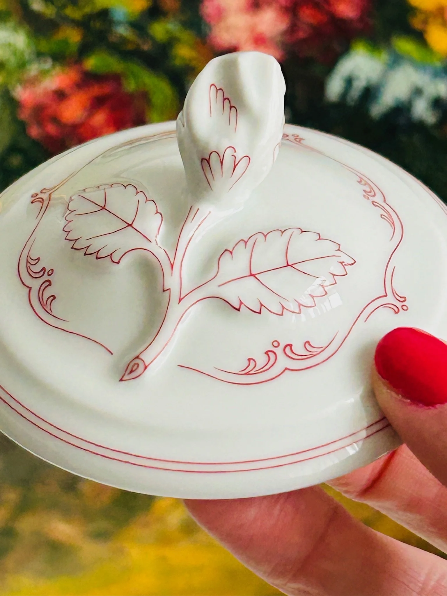 Close-up of the lid decoration and leaf finial, highlighting the delicate red pattern and sculptural porcelain detail.