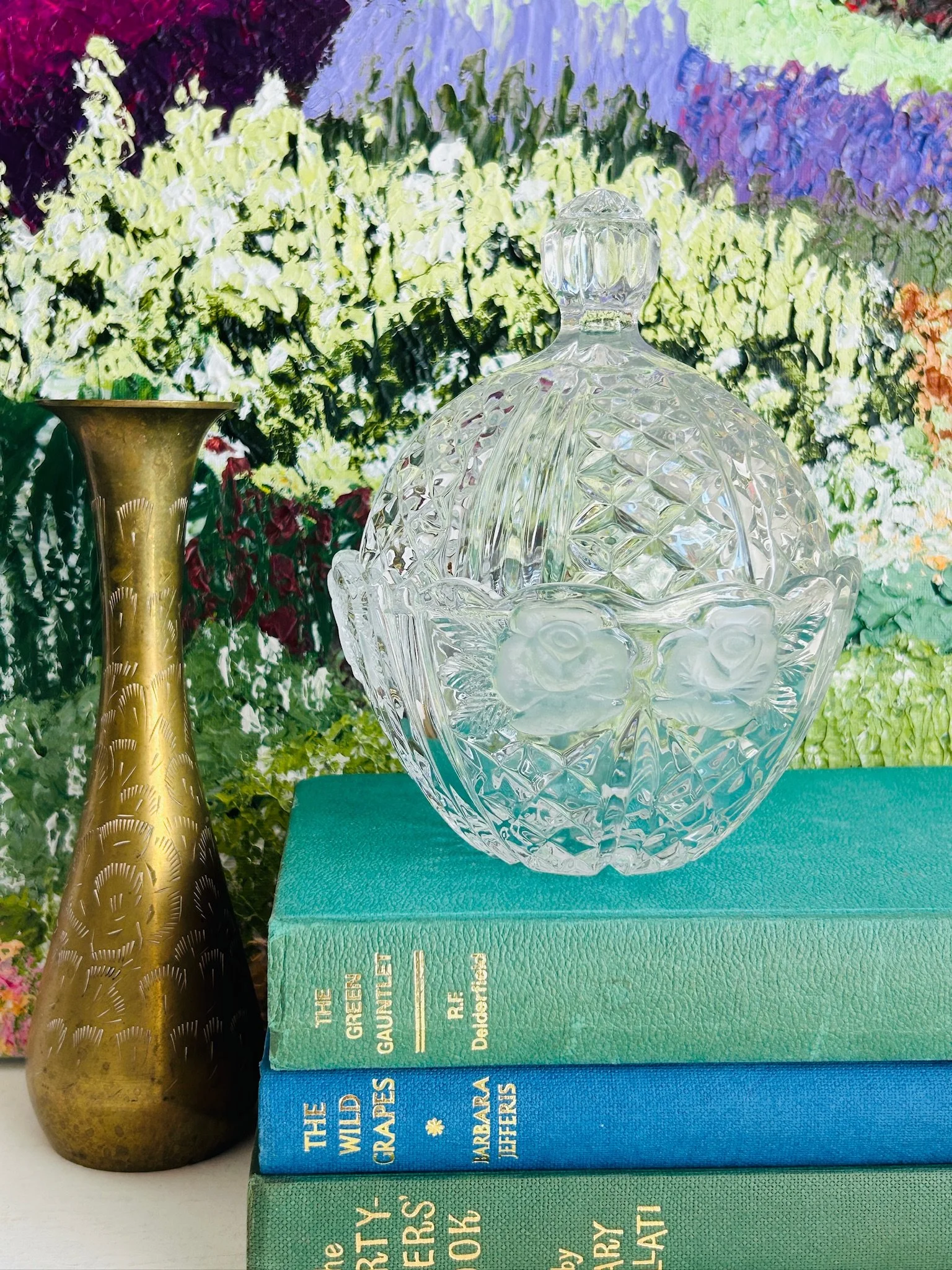 Full display view of the Anna Hütte crystal dish with lid placed on stacked books beside a brass candlestick, styled as vintage home décor.