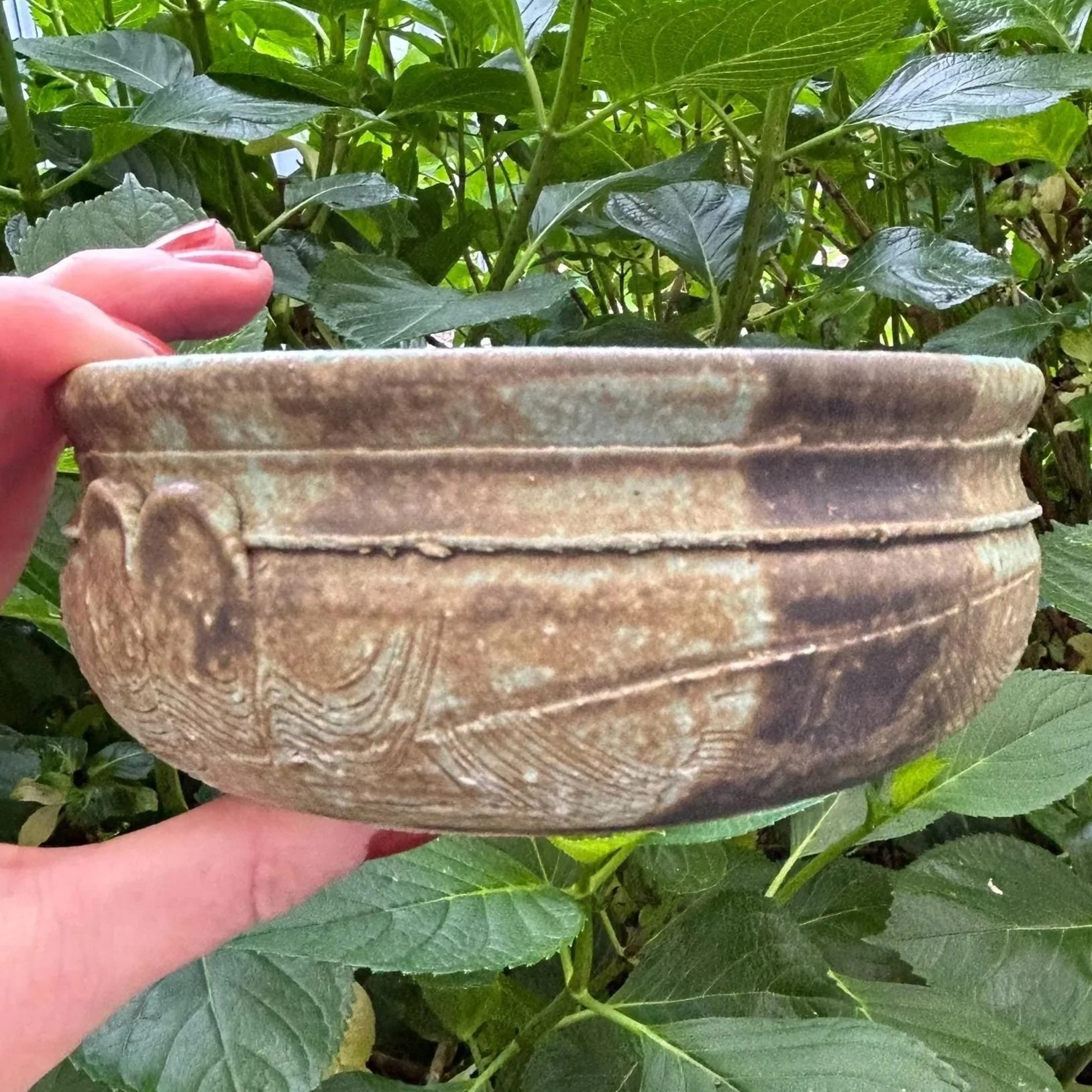 Side profile view of bowl in hand against greenery