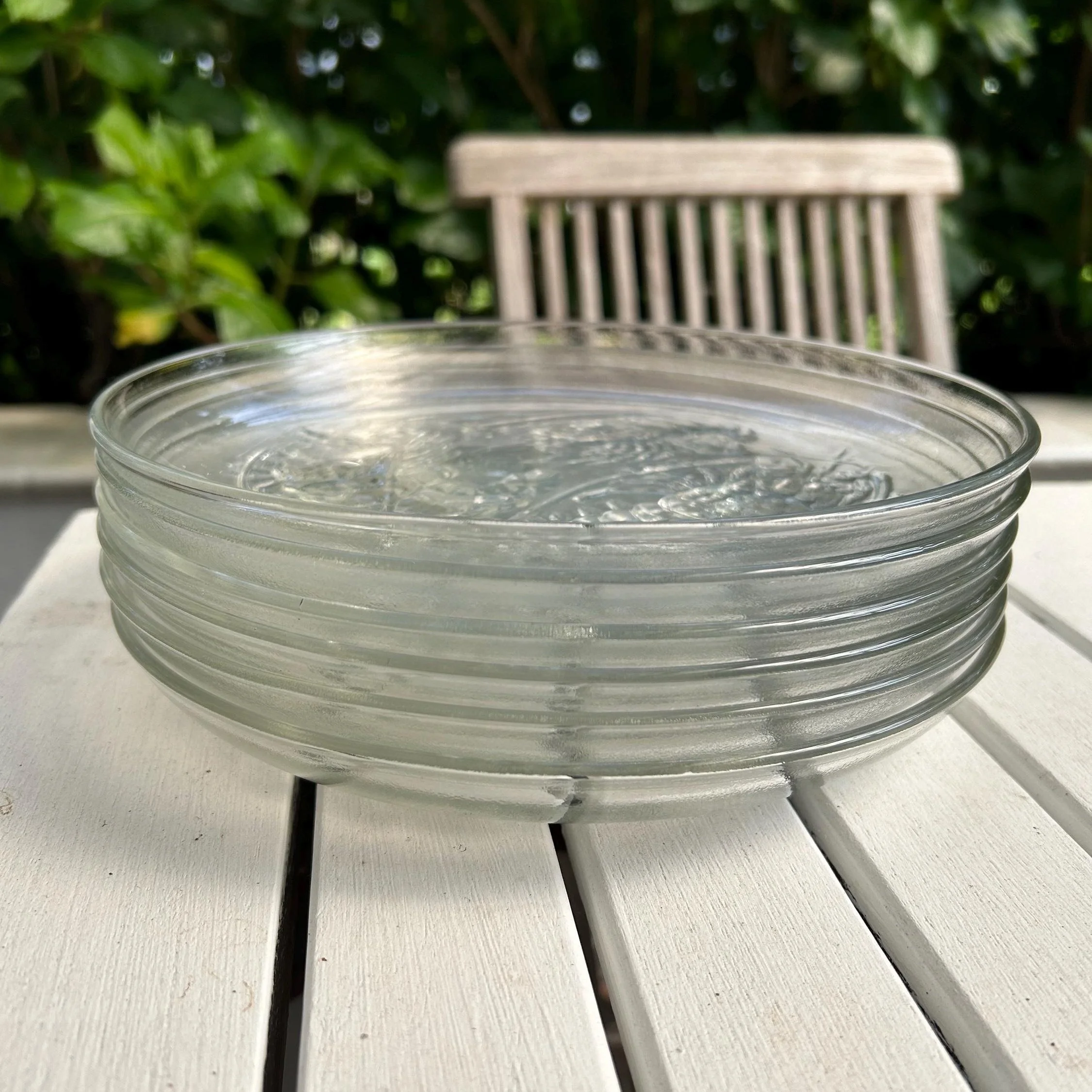 Stacked set of six vintage embossed glass seafood plates on a white outdoor table
