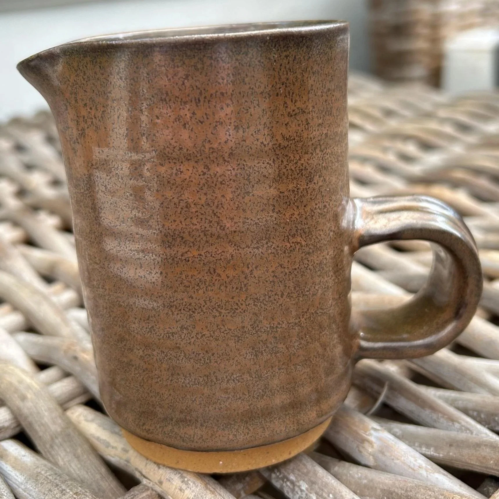 Full side view of ceramic creamer with earthy brown glaze and spout