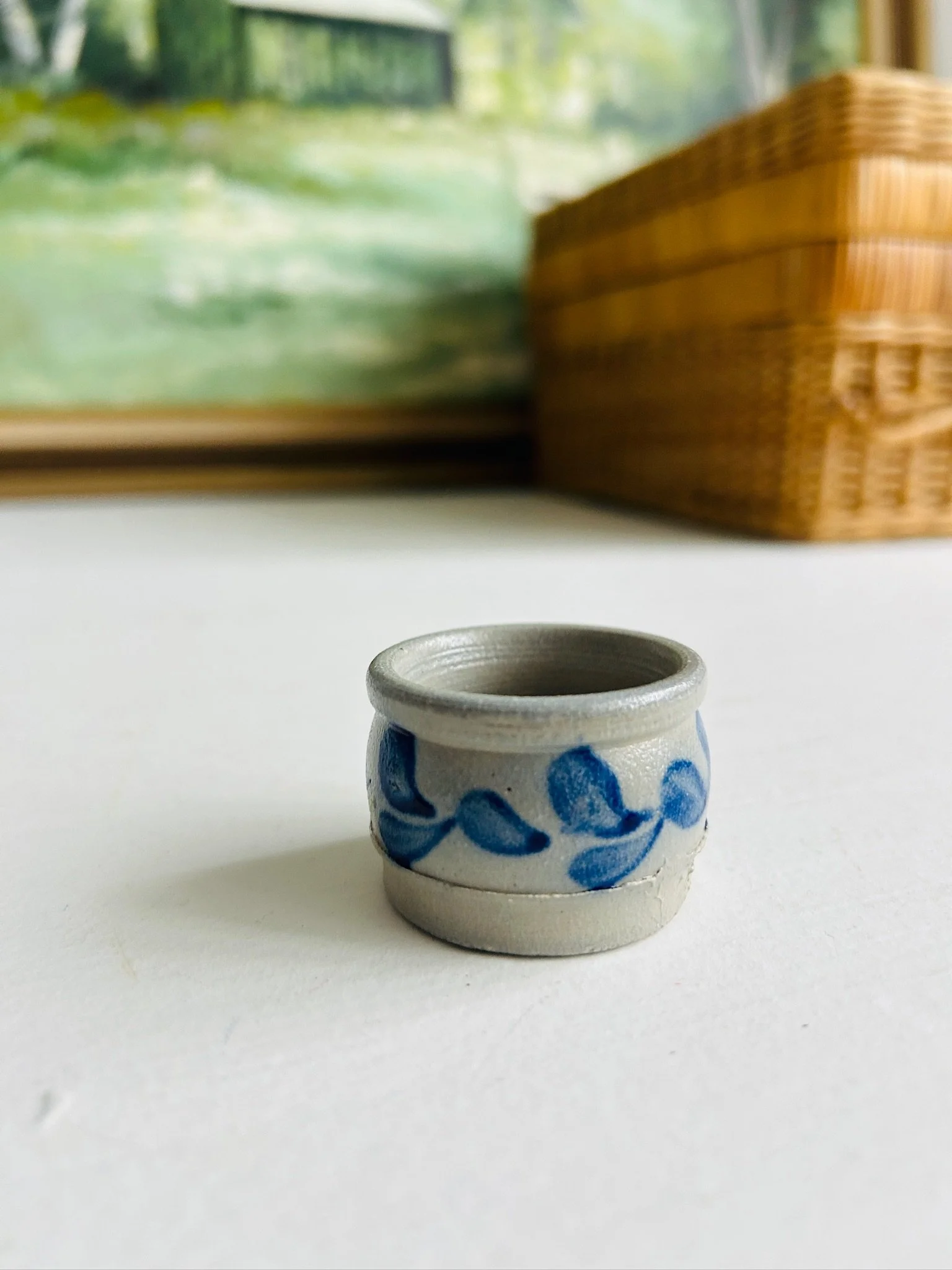 Distant front view of the tiny handmade salt cellar on a white surface beside a wicker basket