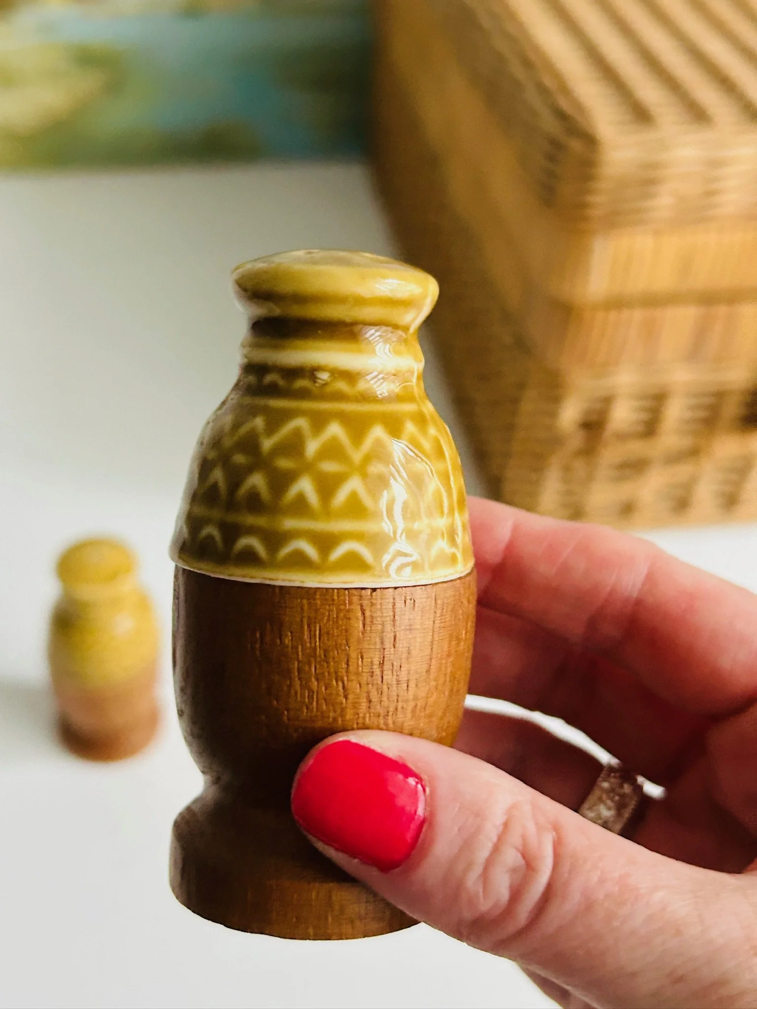 Close-up of a single shaker held in hand, highlighting the mustard yellow geometric ceramic top and wood base