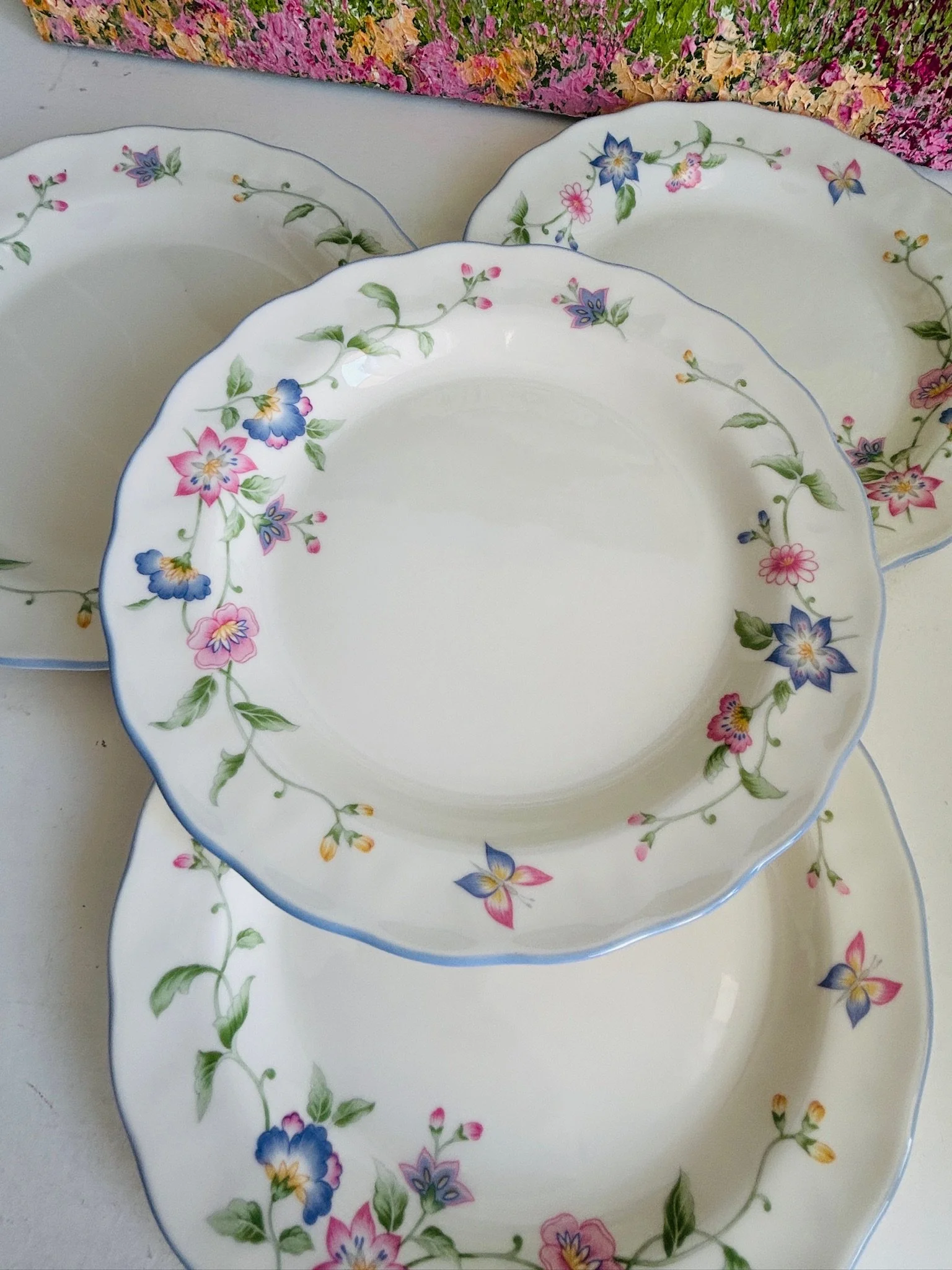 Overhead view of one Royal Doulton RD129 floral plate stacked over matching plates, showing pastel flowers, butterfly detail, scalloped edge, and pale blue rim.