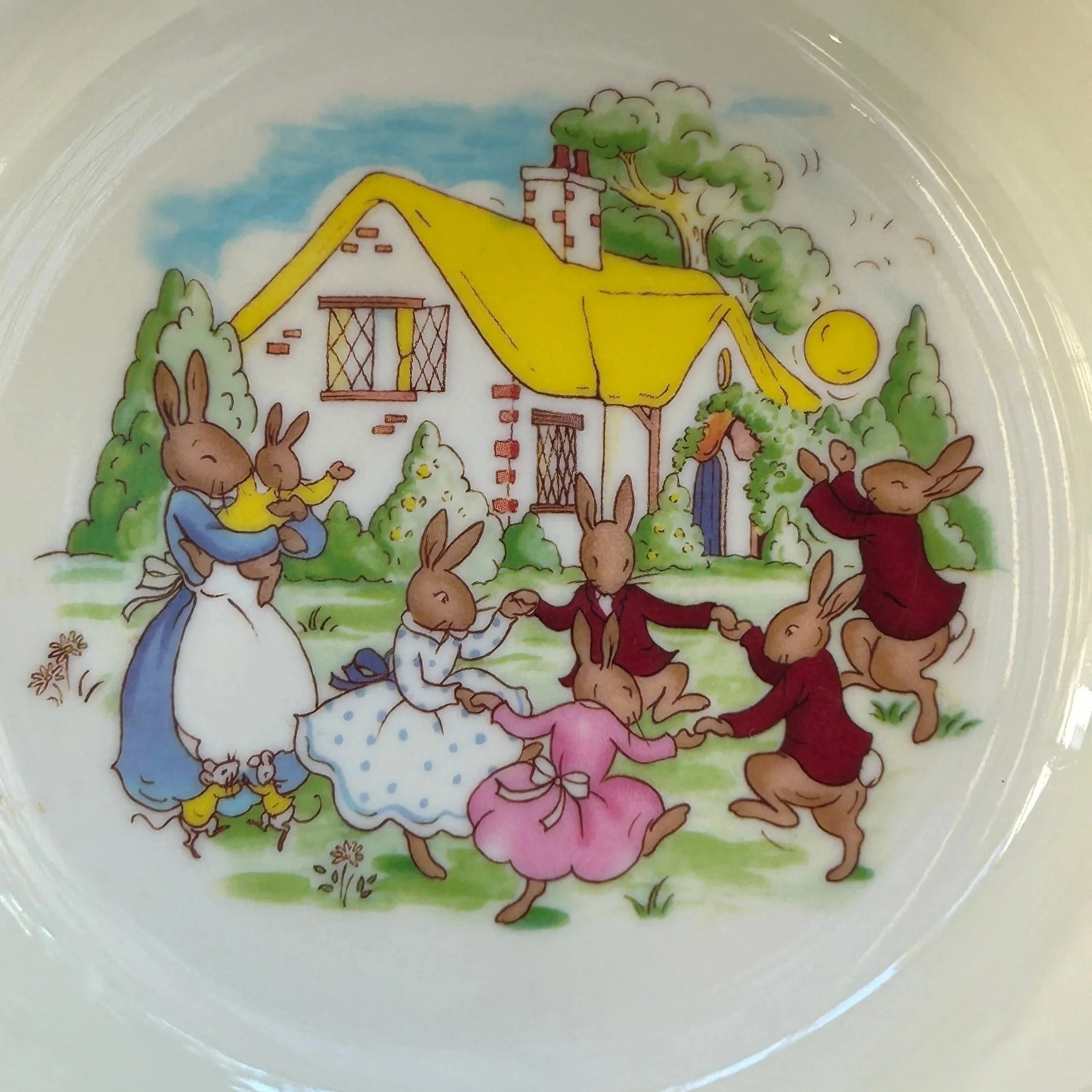 Close-up of Bunnykins scene inside bowl featuring rabbits dancing outside a cottage with a yellow roof