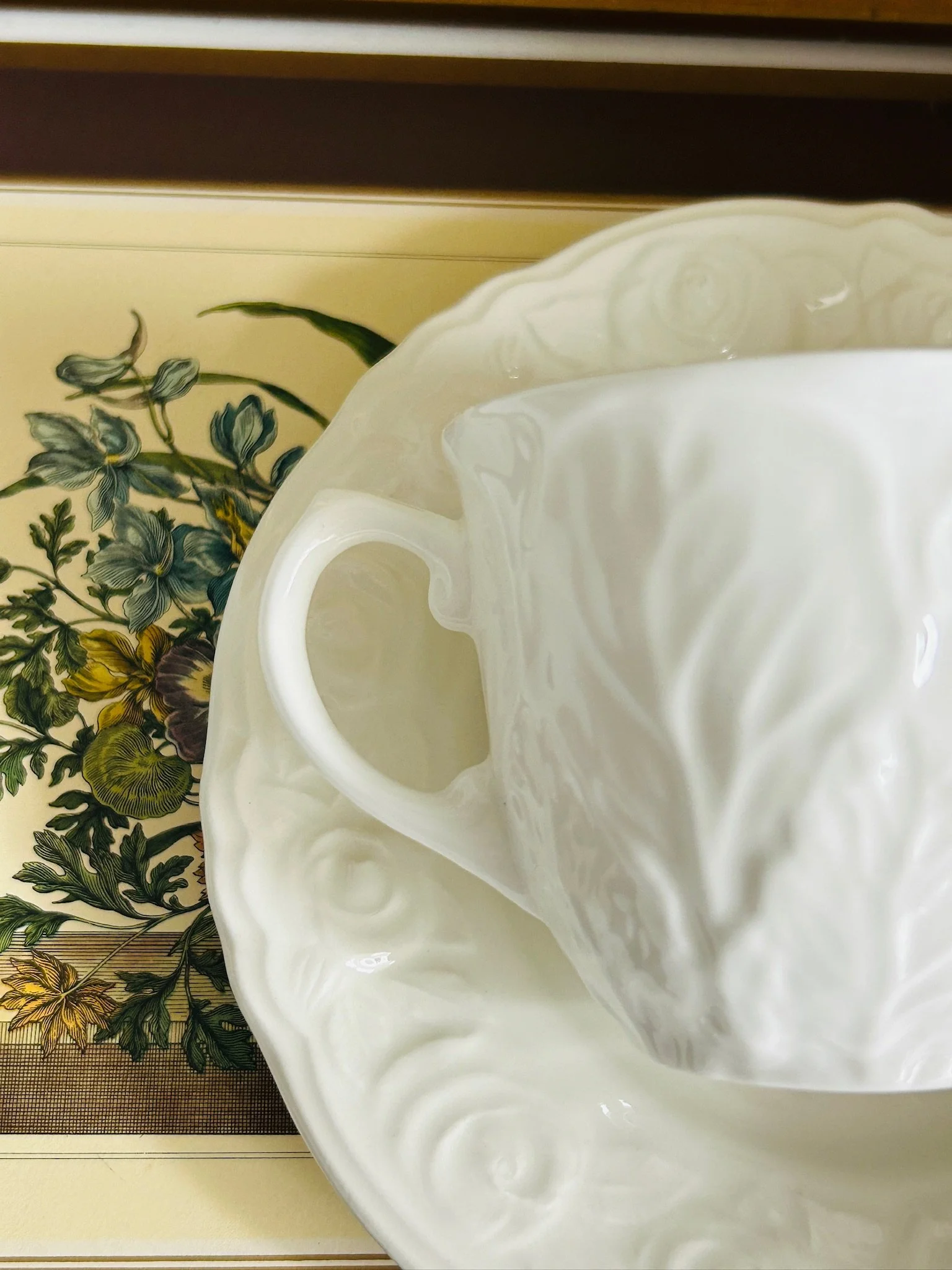 Top-down close-up of the cup handle resting on the embossed saucer, highlighting the glossy white porcelain and raised floral detail.