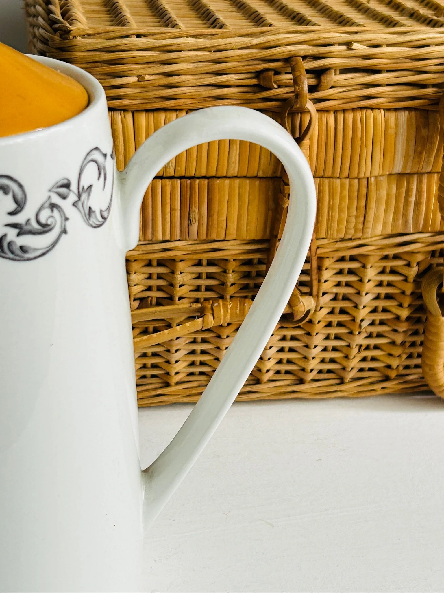 Close-up of the curved white handle against the wicker background, highlighting the graceful shape and glossy earthenware finish.