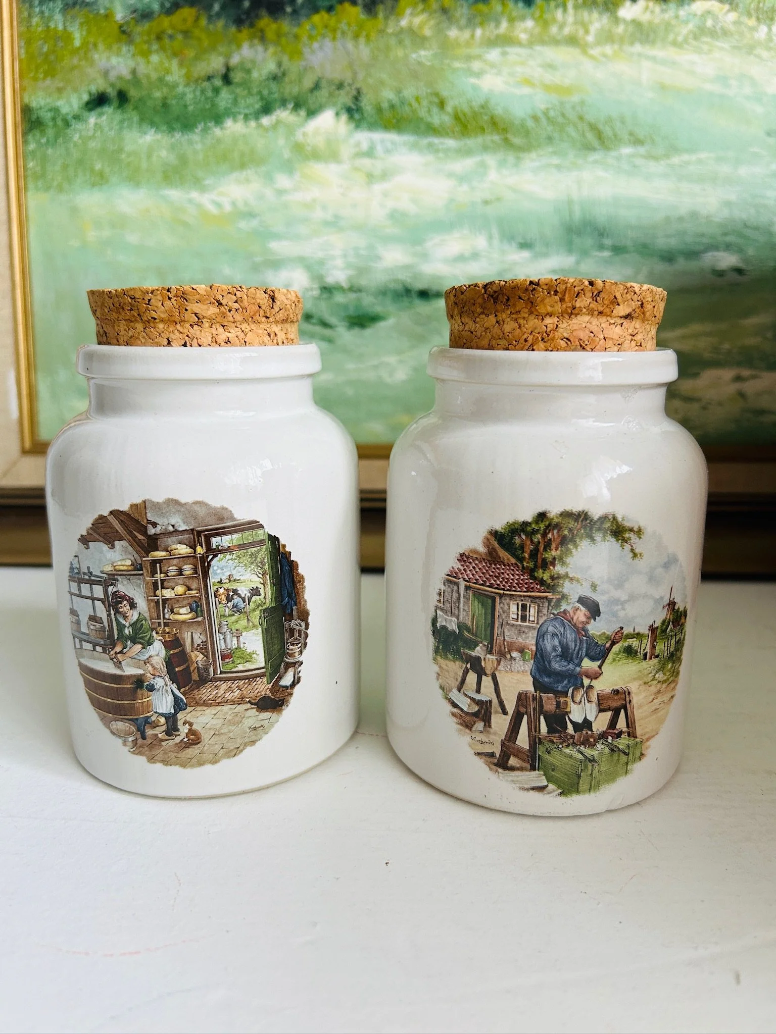 Pair of handcrafted ceramic mustard pots with cork lids, displayed together to show the full set and both illustrated village designs.