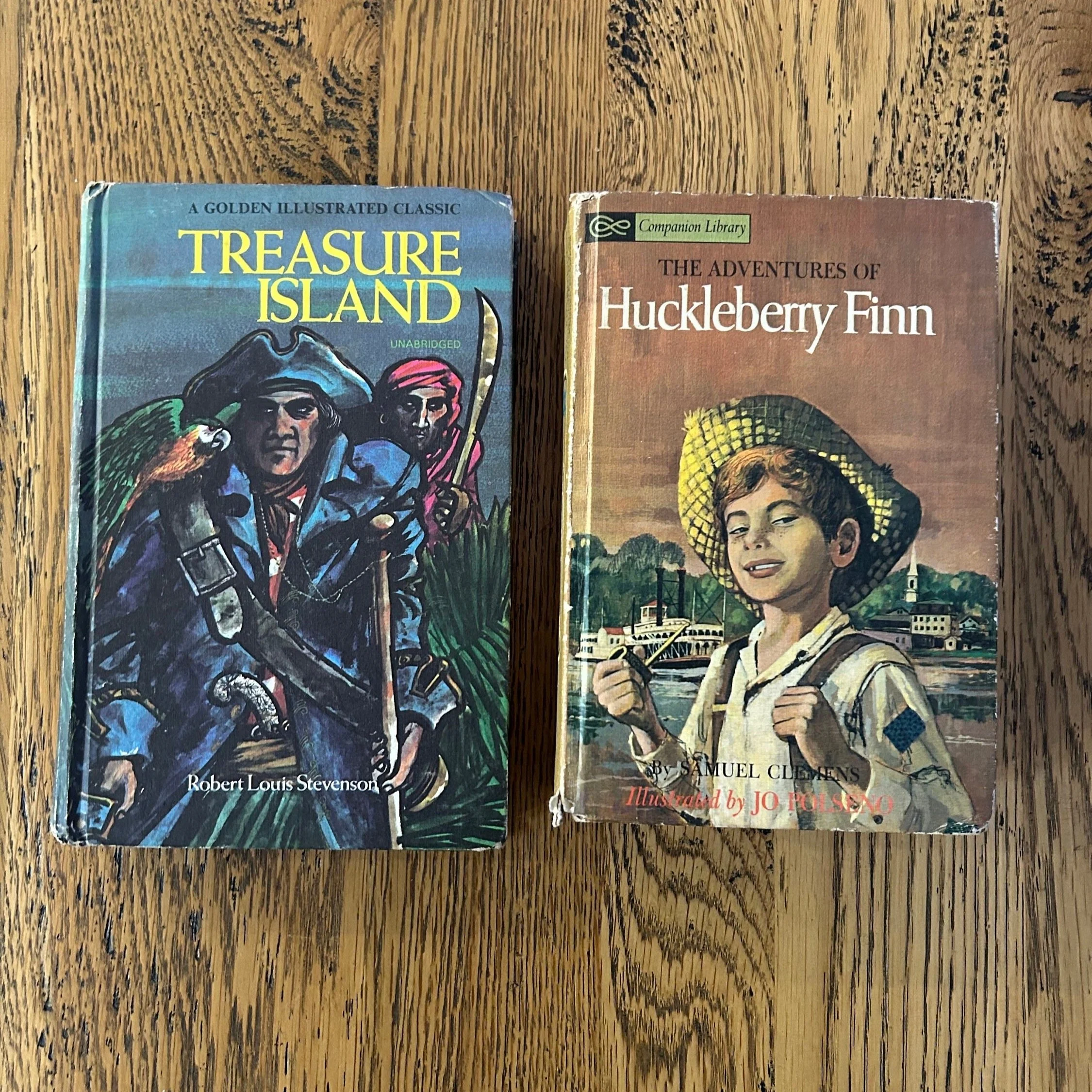 Front covers of vintage hardcover books: 'Treasure Island' and 'The Adventures of Huckleberry Finn' from Companion Library collection