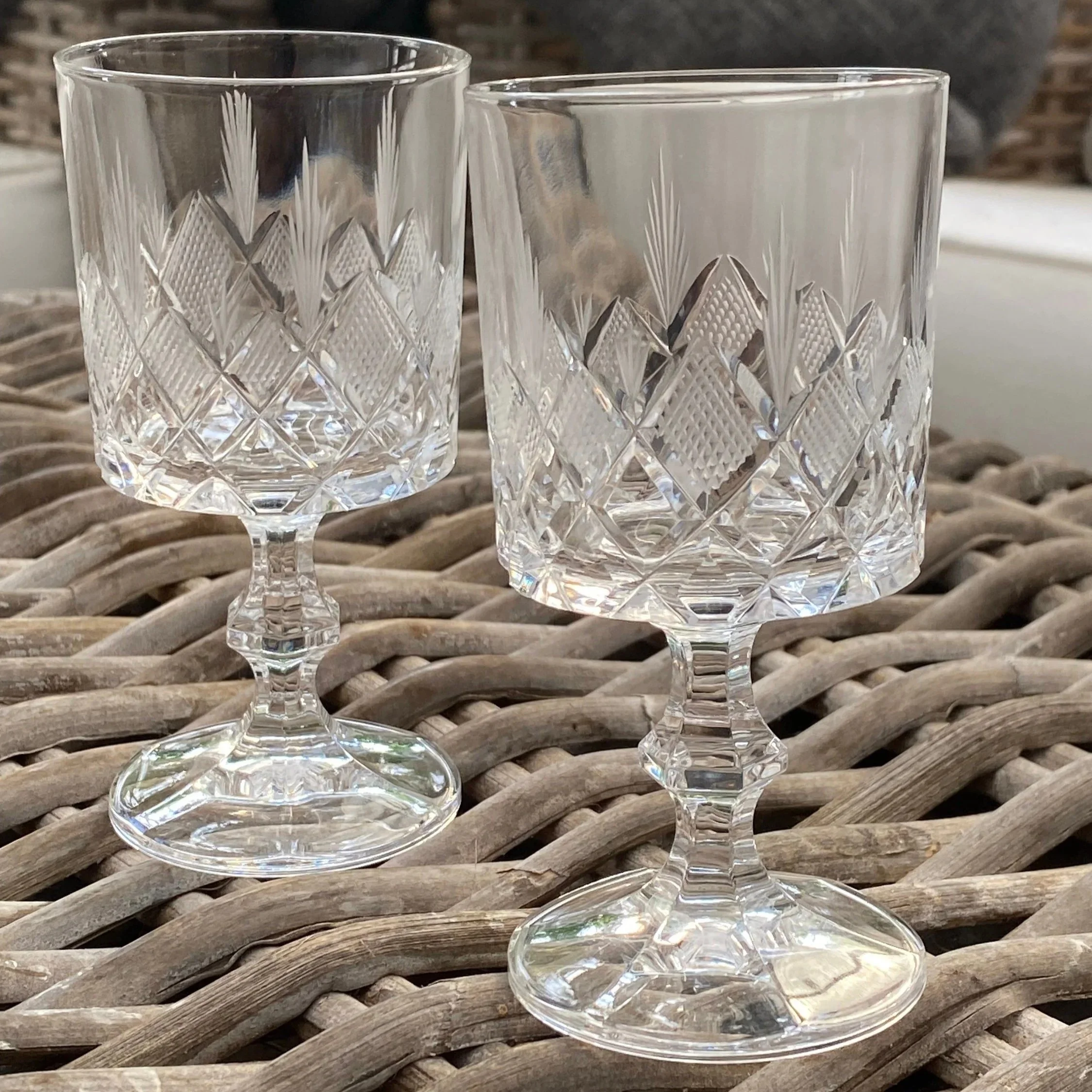 Pair of vintage etched stemmed glasses on wicker table in natural light