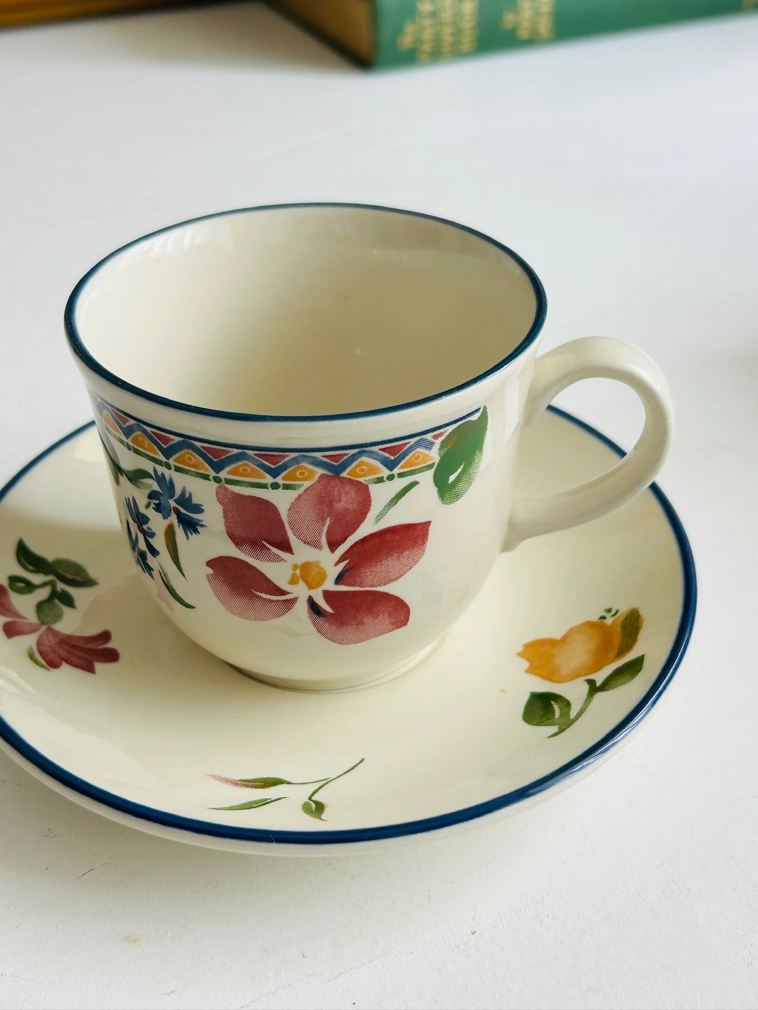 Side view of the Staffordshire ‘Calypso’ tea cup resting on its matching saucer, highlighting the curved handle, floral pattern, and blue-edged rims.