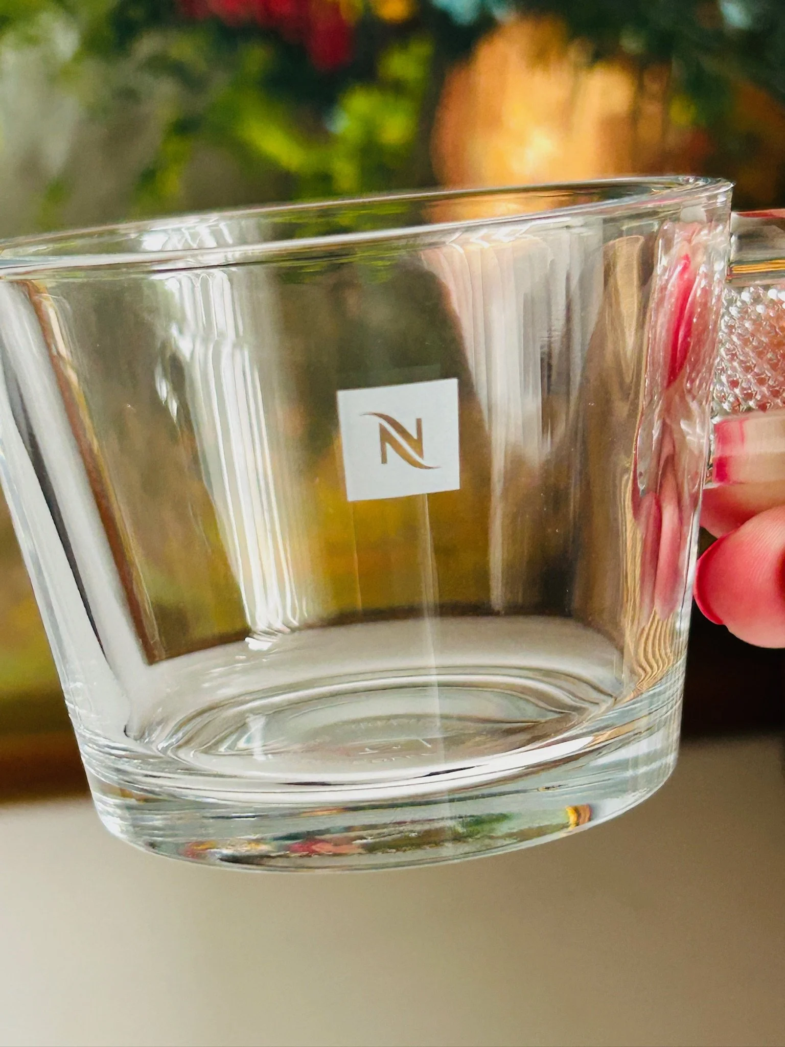 Close-up of a single clear glass Nespresso cup showing the etched logo and tapered shape