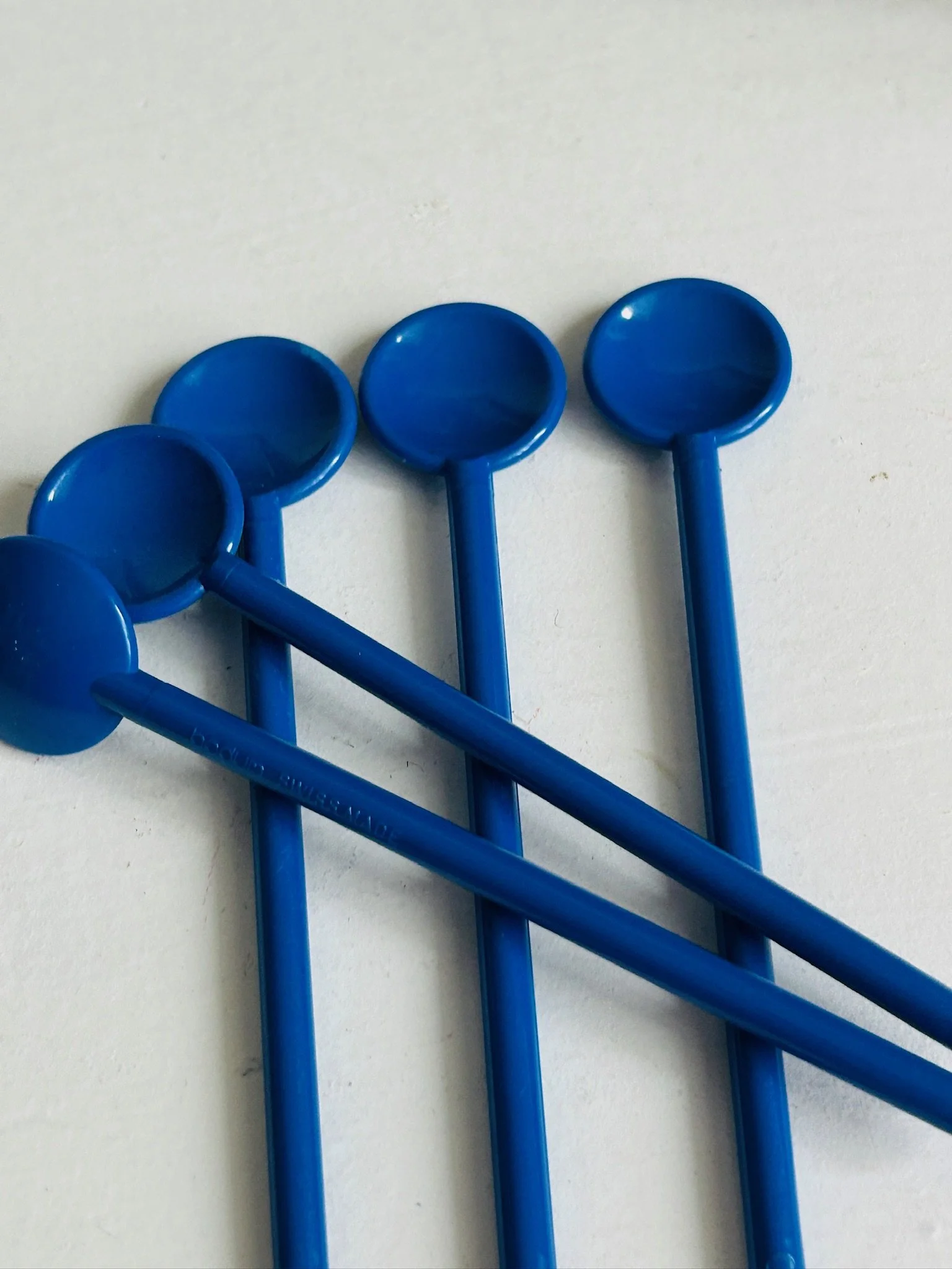 Five cobalt blue plastic Bodum stir spoons laid out flat, showing their round spoon heads and straight handles