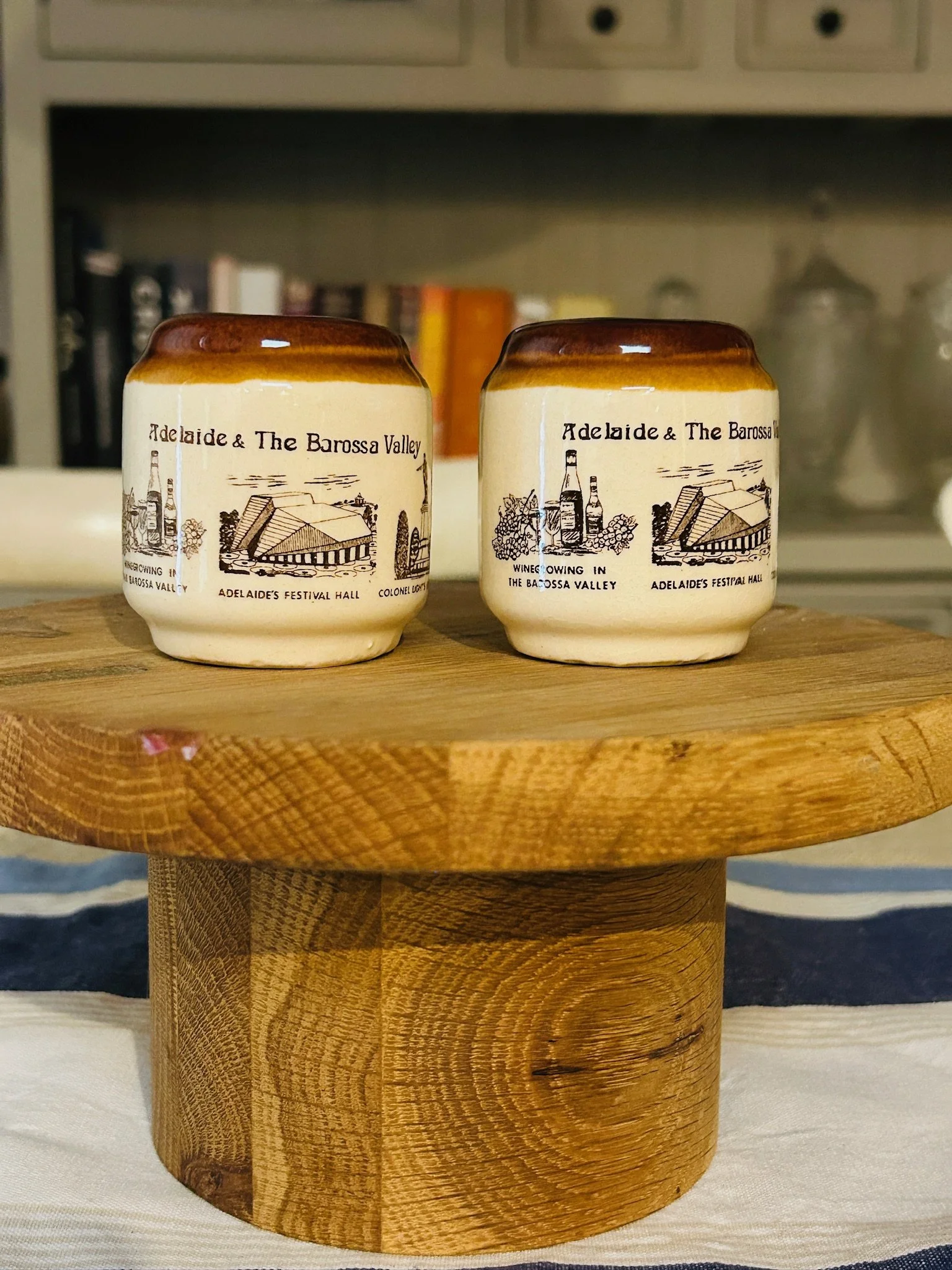 Pair of vintage stoneware salt and pepper shakers on a wooden stand, featuring cream bodies, brown drip-glaze tops, and Adelaide and Barossa Valley souvenir illustrations.