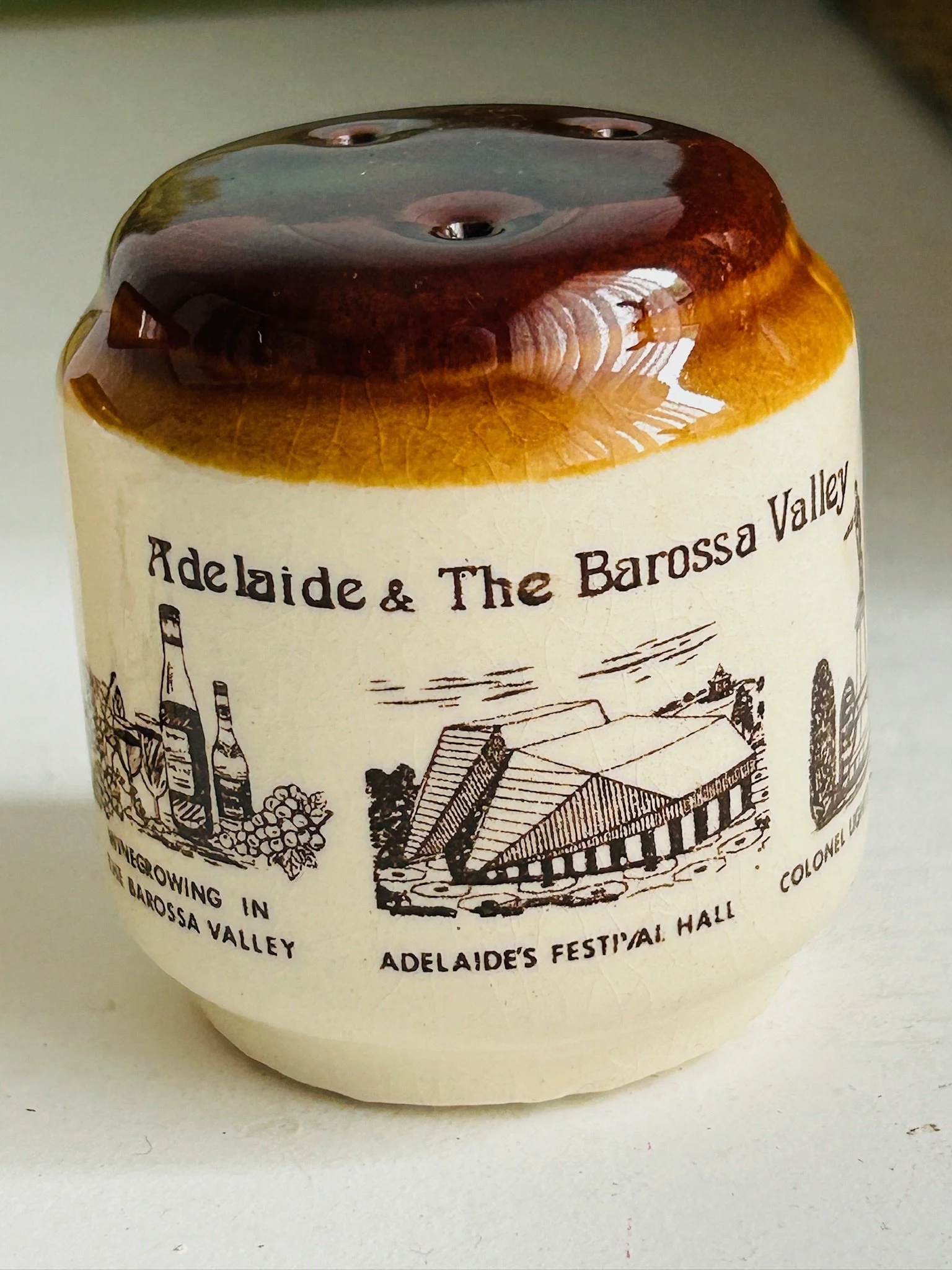 Close-up of one shaker showing the printed Adelaide and Barossa Valley illustration with cream stoneware body and brown drip glaze.