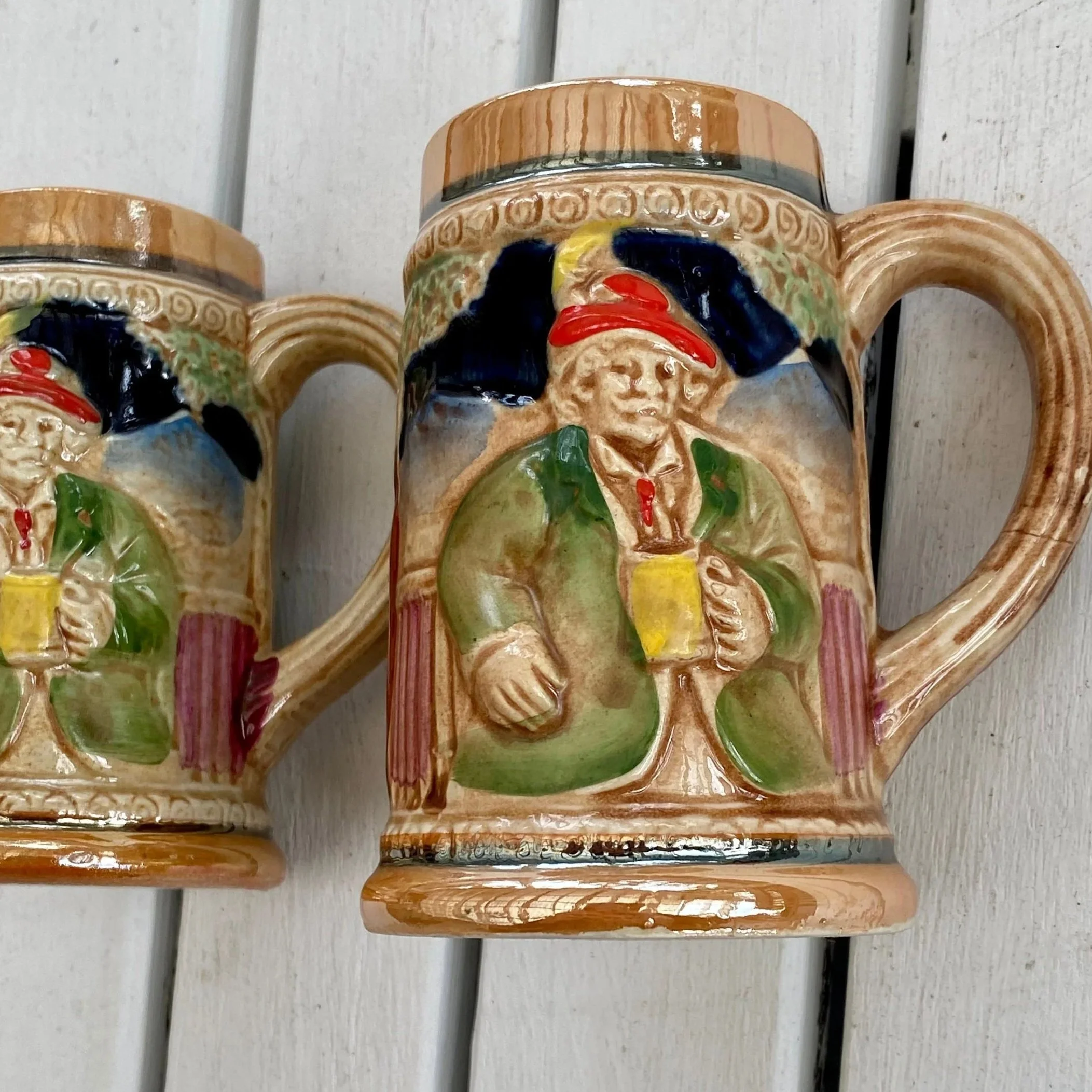 Two vintage 1960s ceramic tankards side by side showing the front relief design of a man holding a drink.