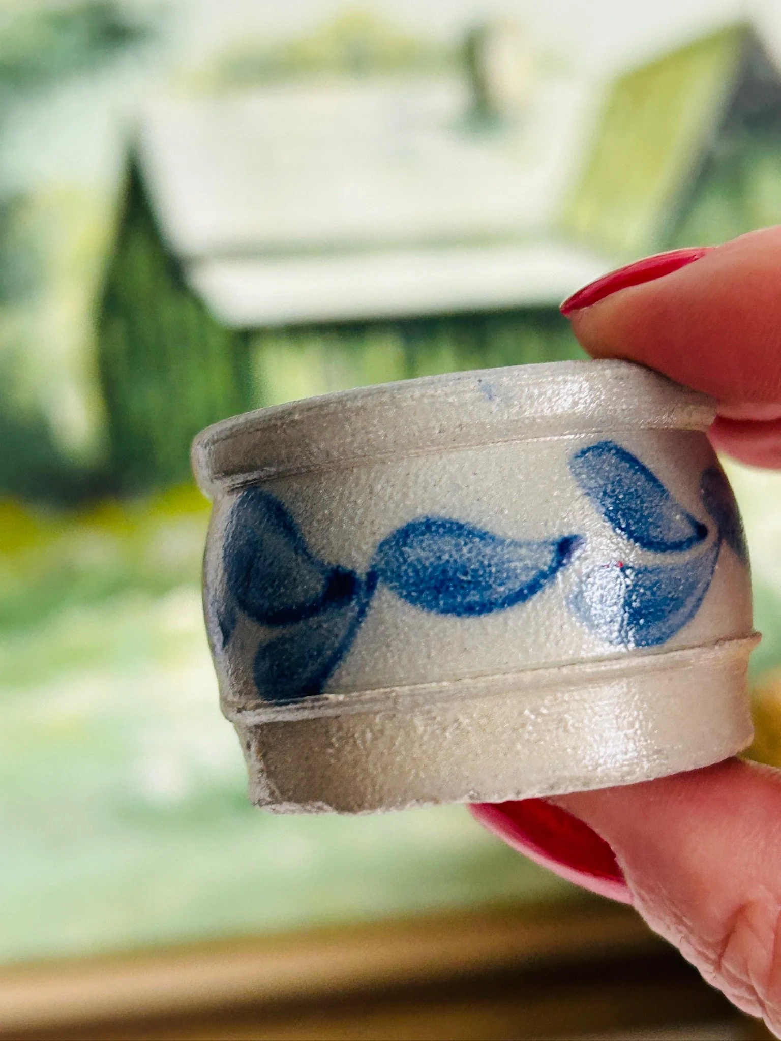 Side view of the salt cellar held between fingers, highlighting the hand-painted cobalt blue leaf pattern and handmade texture