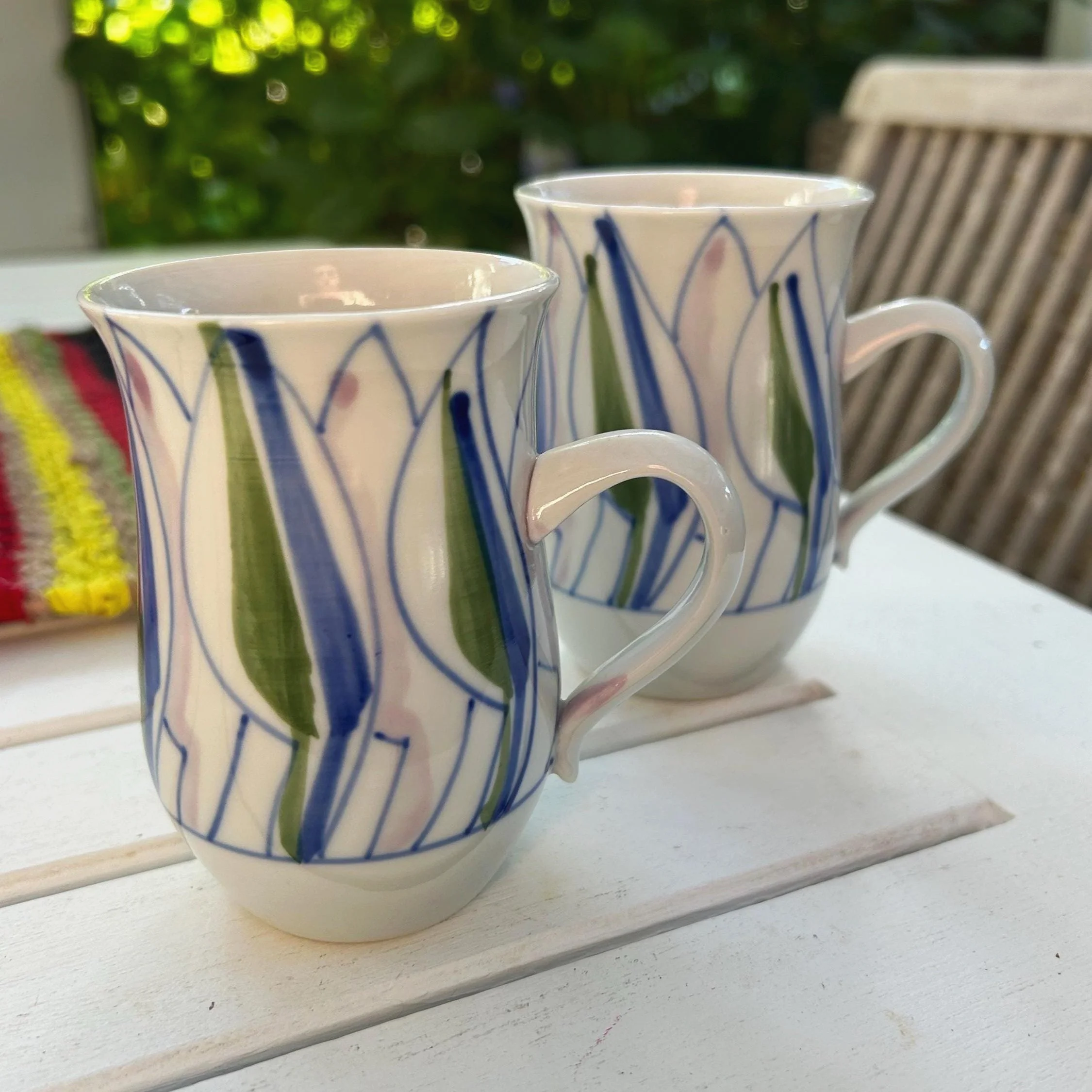 A set of two hand-painted porcelain mugs by Alistair Whyte, showcasing vibrant floral designs. Signed and crafted in Australia.