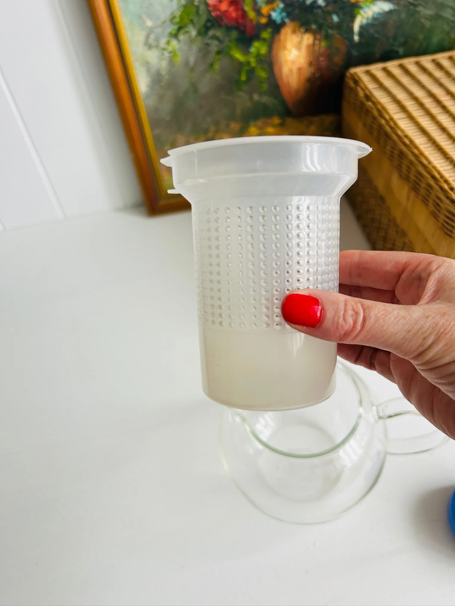 Removable white mesh infuser basket held in hand, showing the perforated surface and pale base.