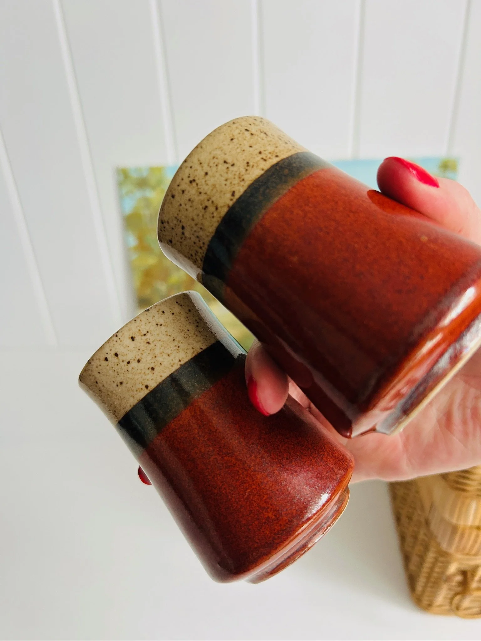 Two tri-tone ceramic shakers held in hand, showing their tapered shape and glossy reddish-brown glaze.