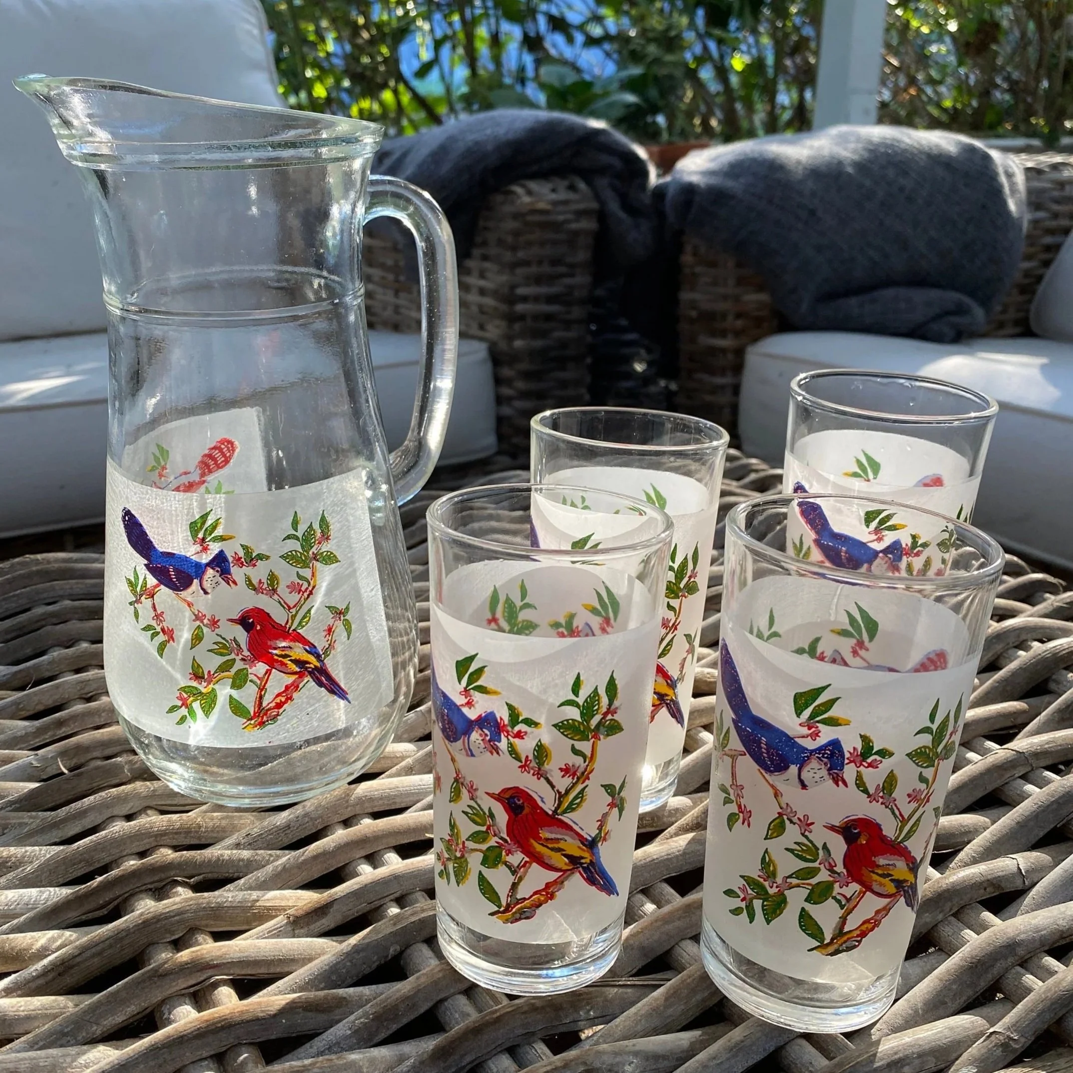 Side view of water jug with bird motif and glasses on wicker surface