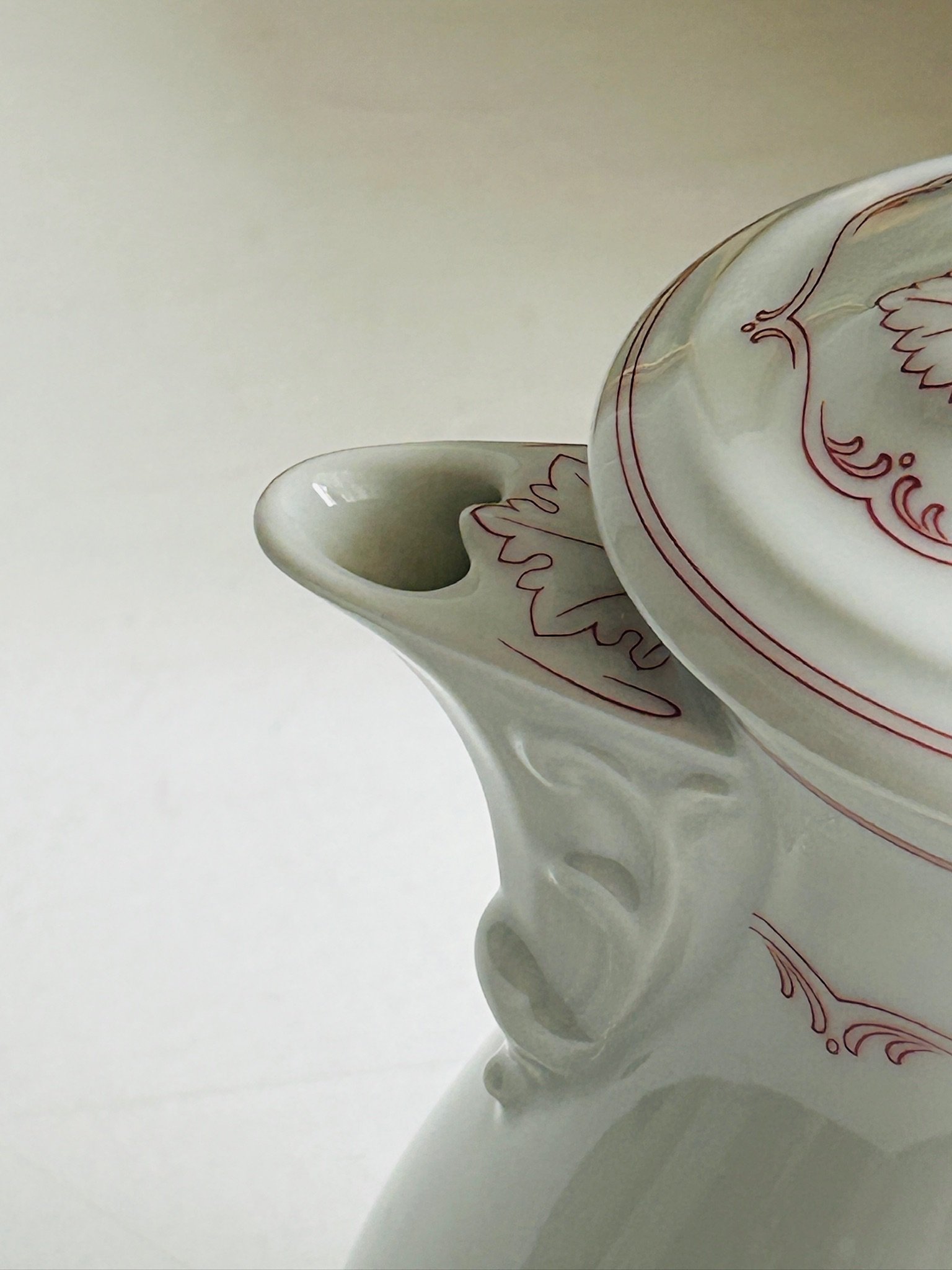 Detail of the sculpted pouring spout and lid edge, showing the elegant relief work and fine red line decoration.