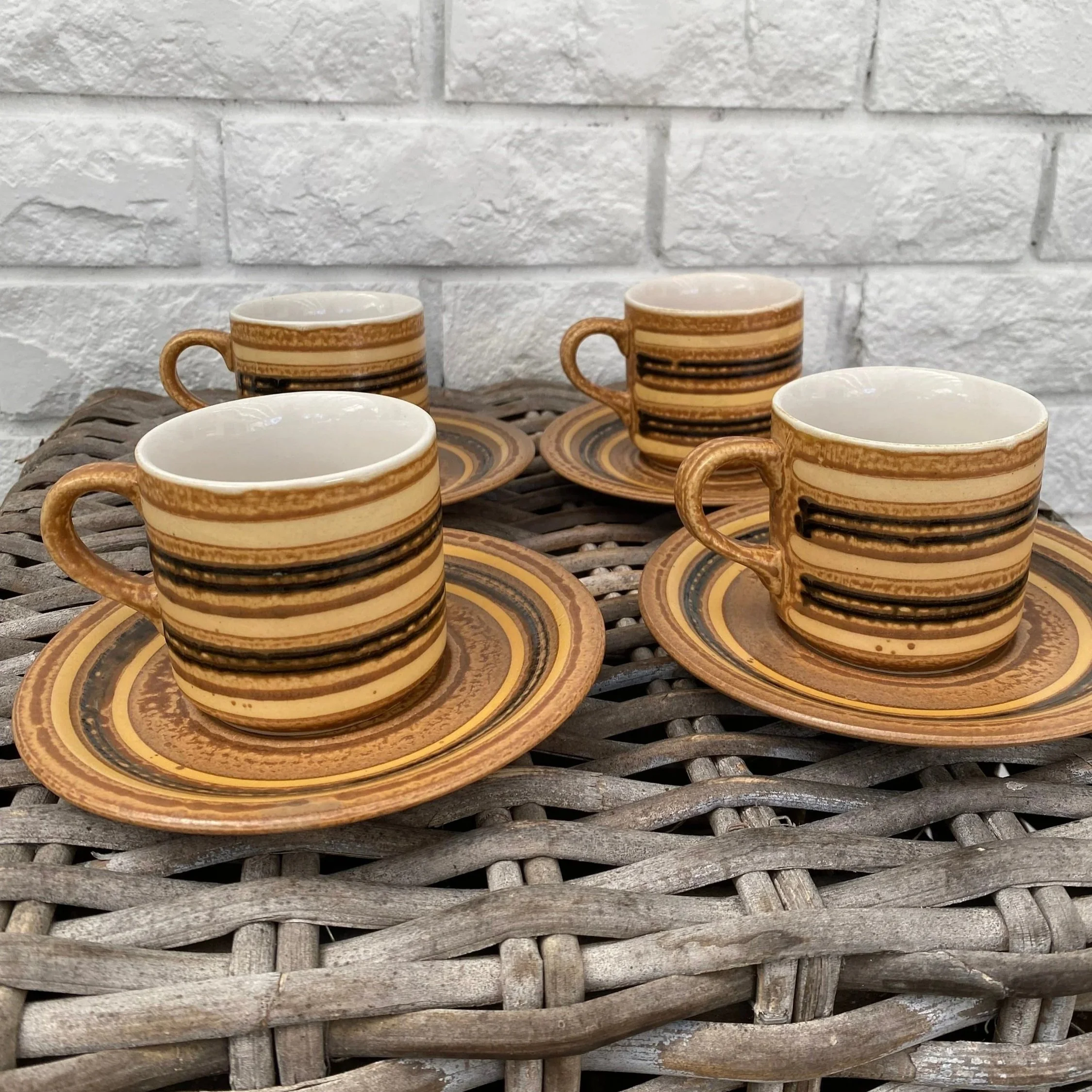 Group of four cups and saucers styled in front of a white brick wall