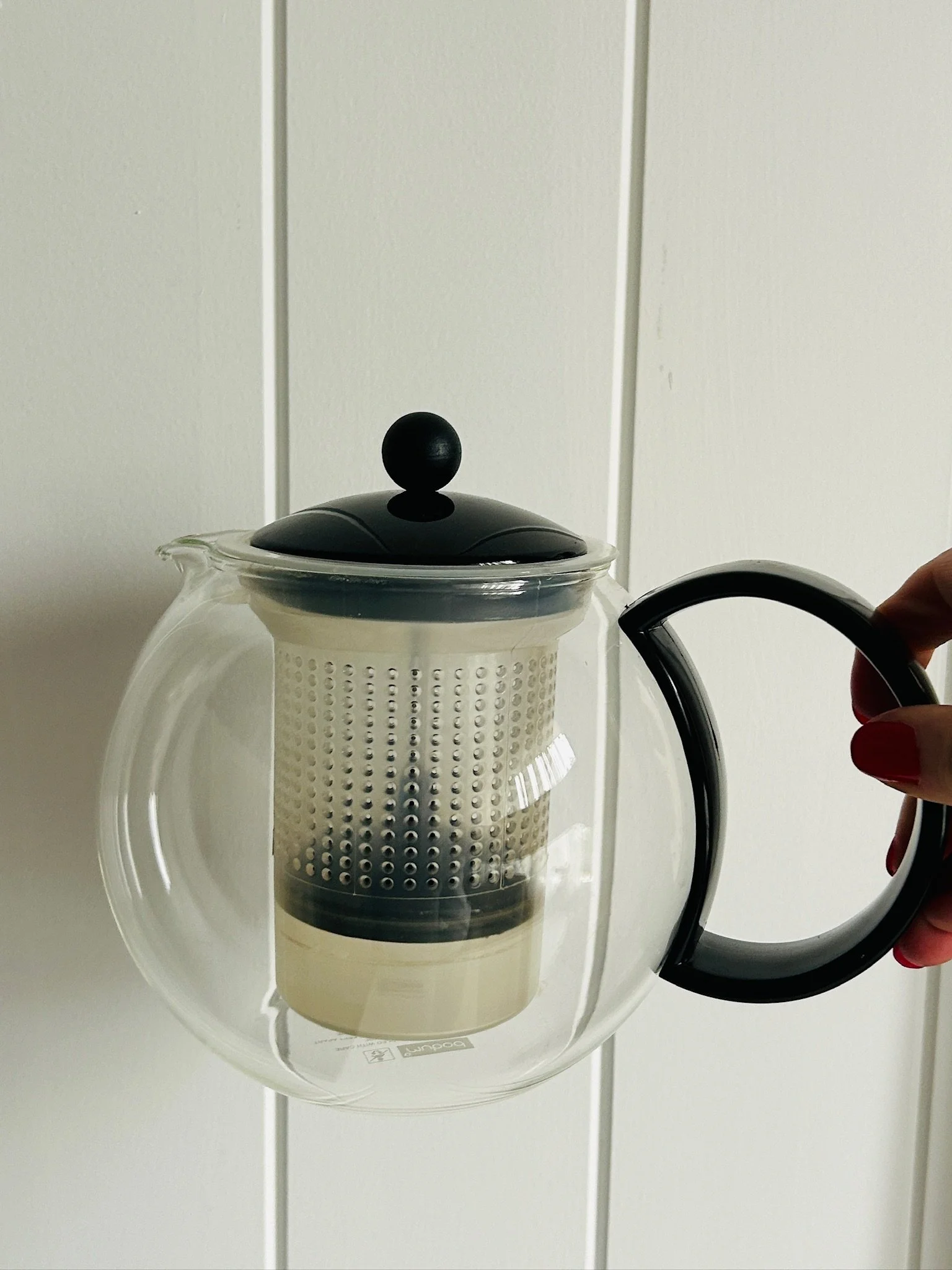 Front-facing view of the tea press held by the black handle, showing the complete teapot with lid and infuser in place.