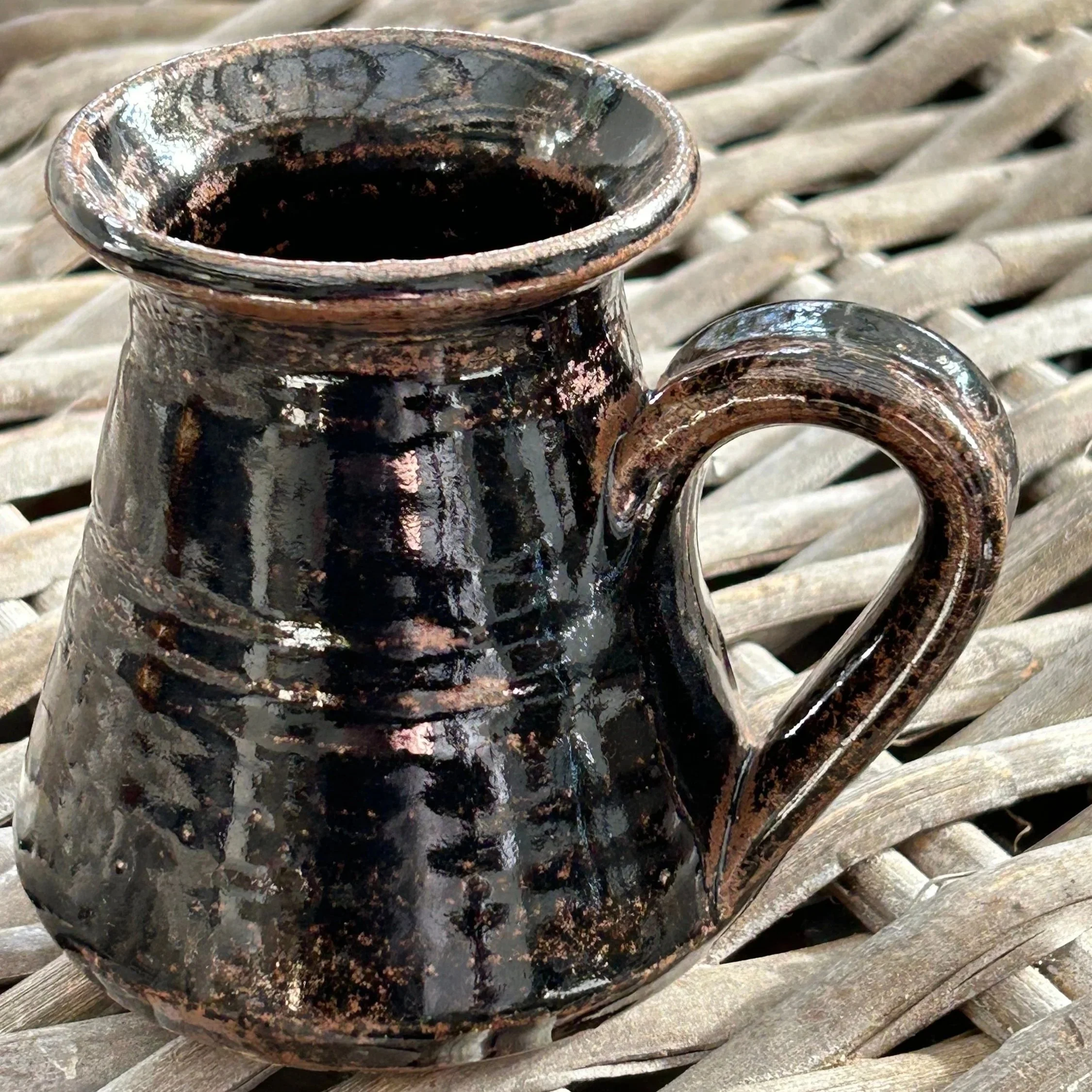 Side view of the handmade black glazed pottery mug with curved handle