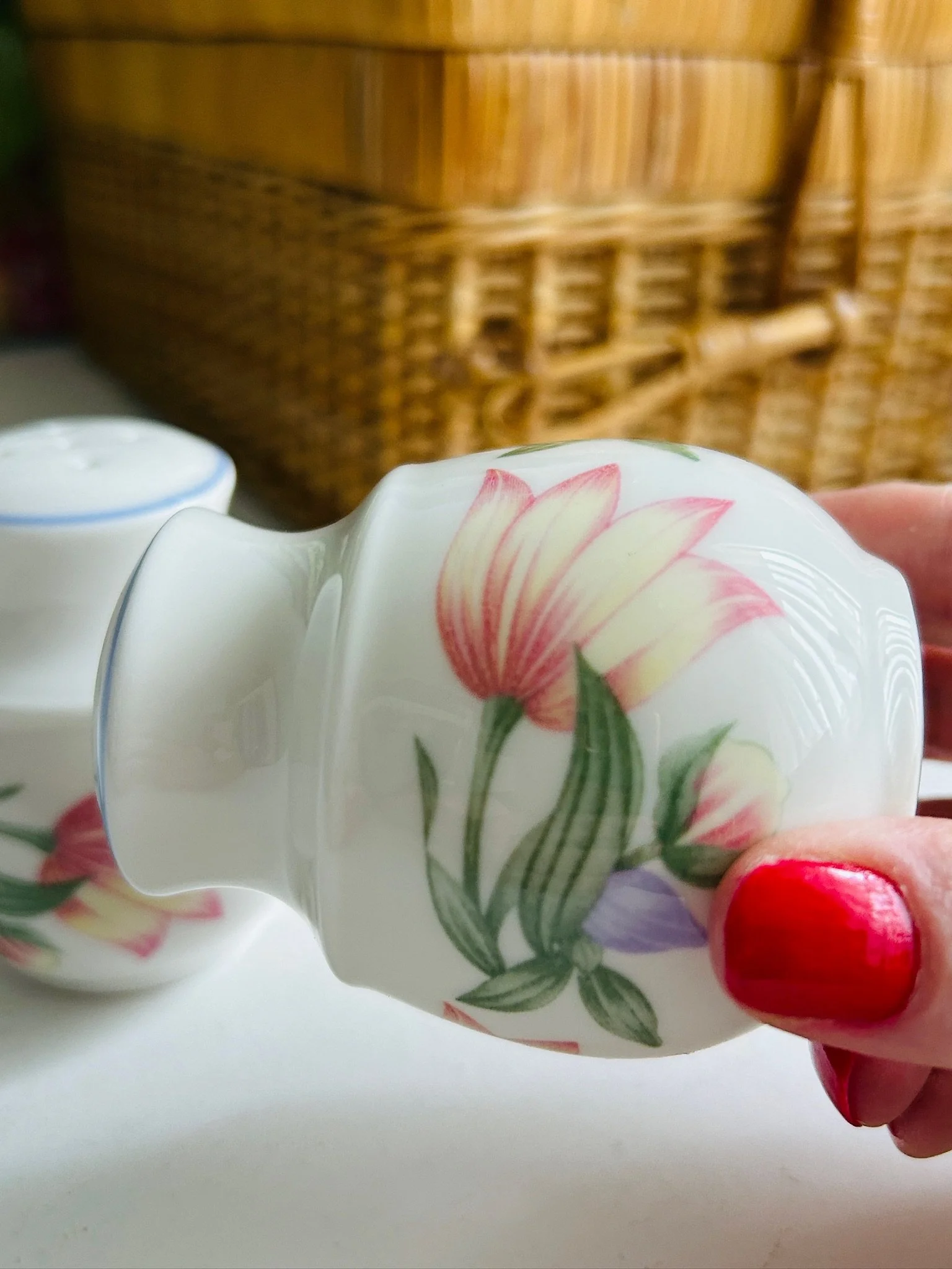 Close-up of one shaker held at an angle, highlighting the pink flower, green leaves, and glossy white china finish