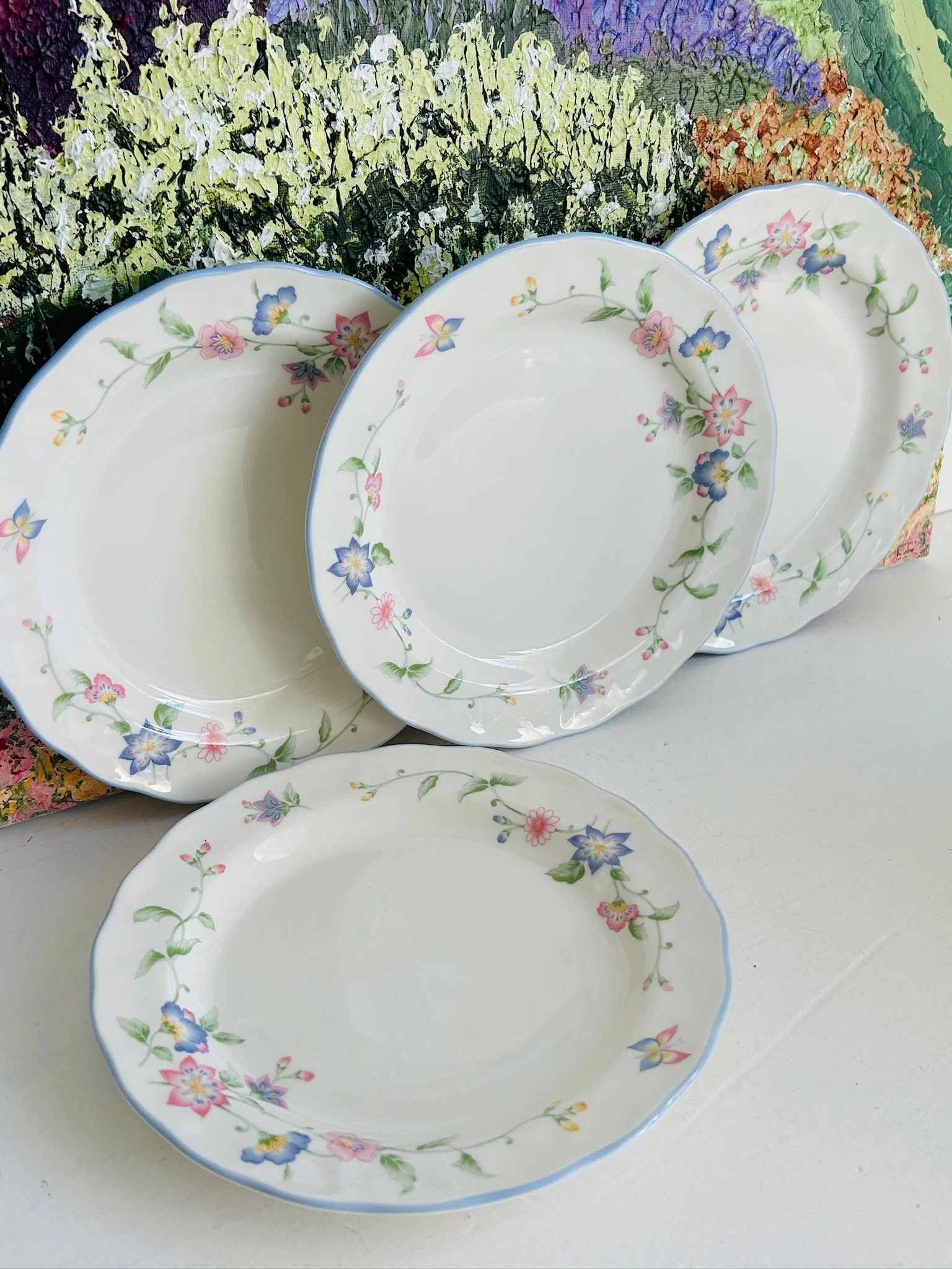 Group view of four matching Royal Doulton RD129 plates arranged upright and overlapping, showing the overall floral pattern and scalloped shape.