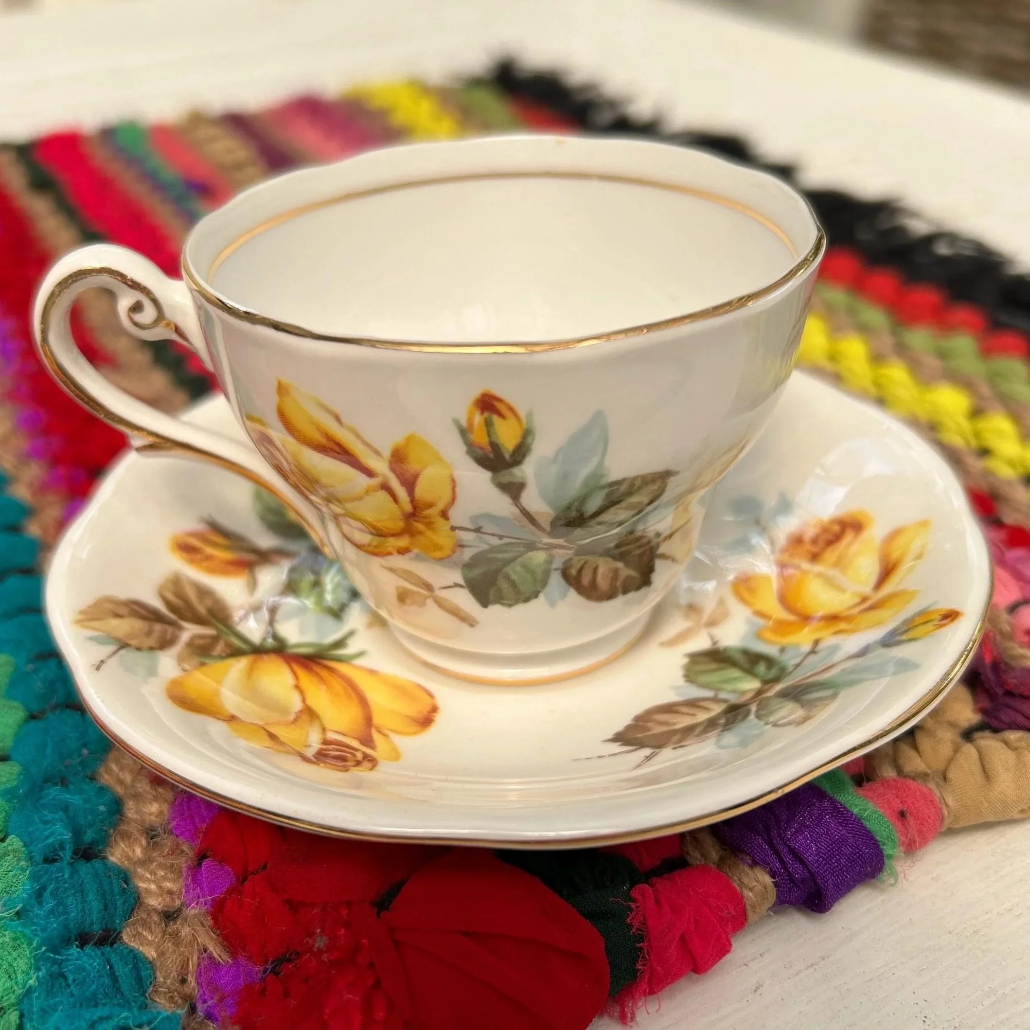 Tea cup and saucer set with yellow rose pattern, displayed on colourful mat
