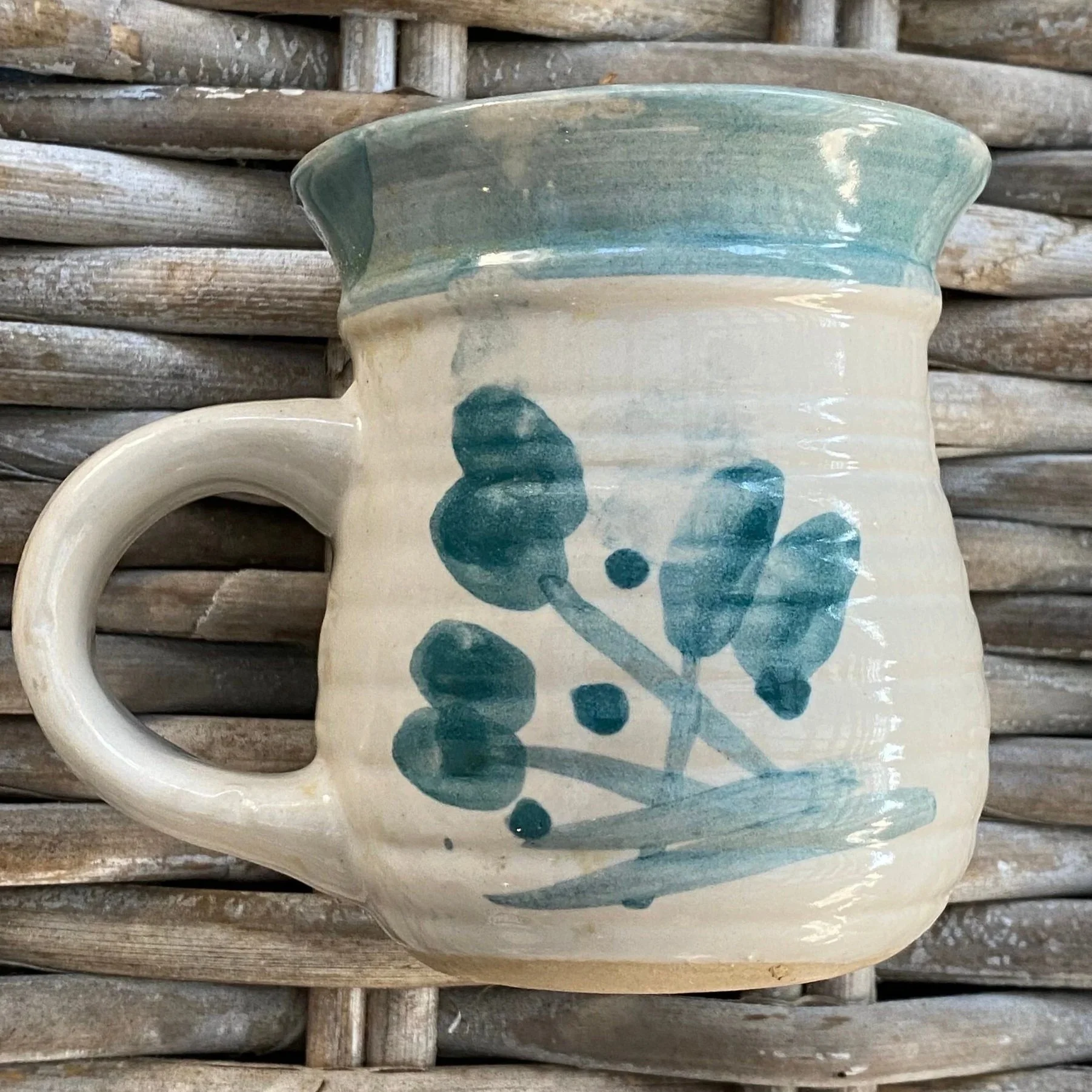 Side profile of cream ceramic mug with teal leaf motif