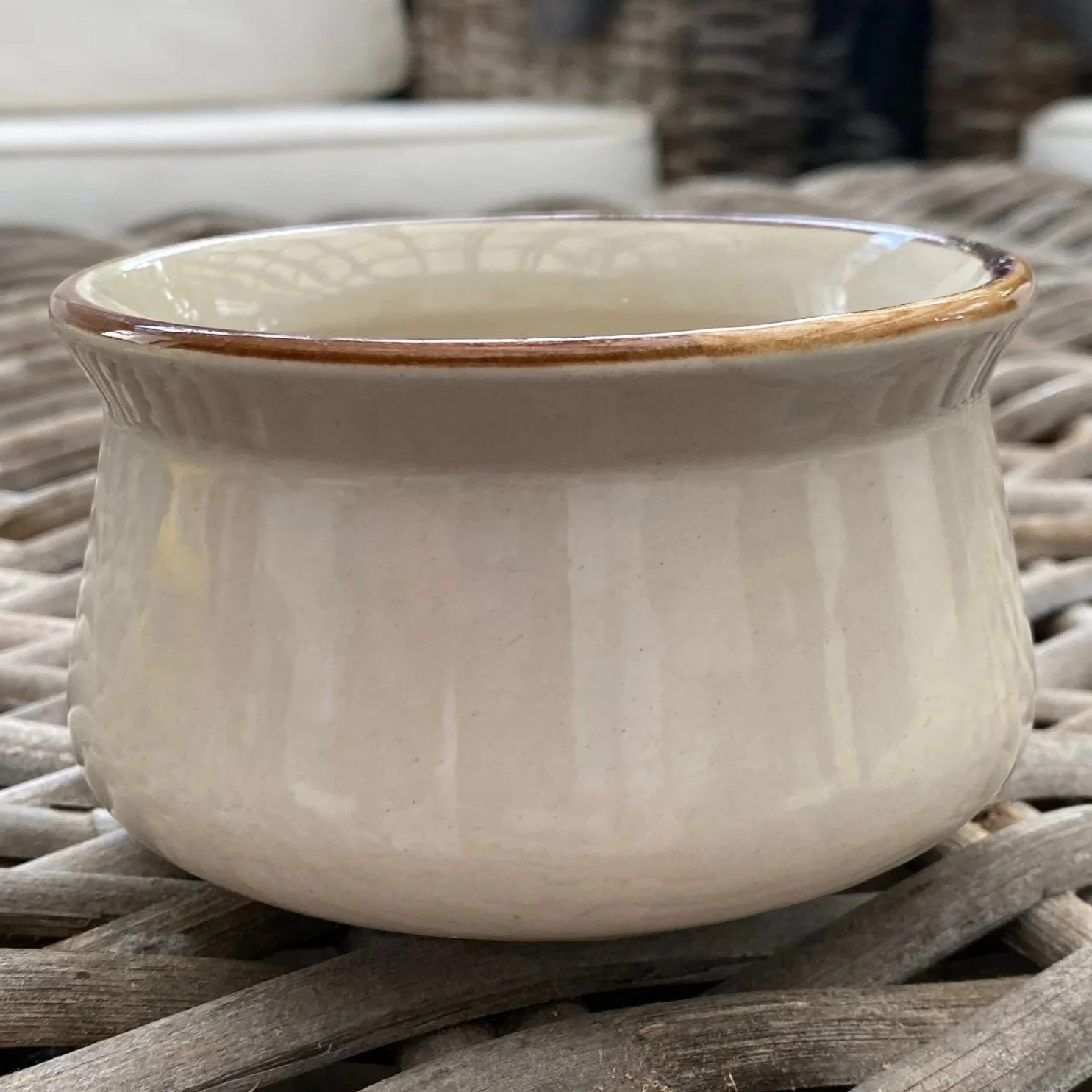 J I Stonecrest ceramic bowl with cream glaze and brown rim on woven surface