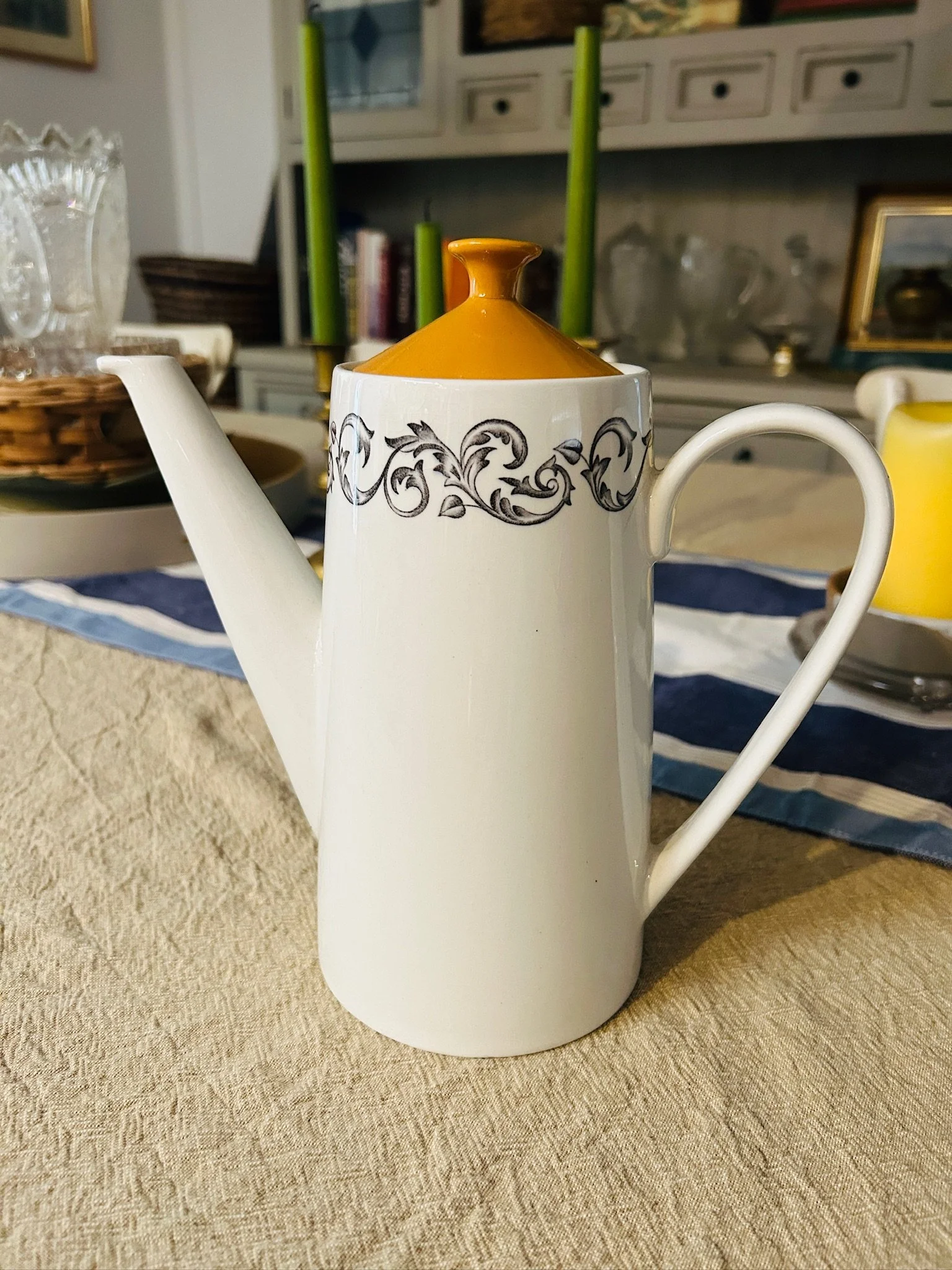 Angled side view of the Johnson Brothers coffee pot highlighting the tall cylindrical shape, curved handle, long spout, black scroll pattern, and orange lid.