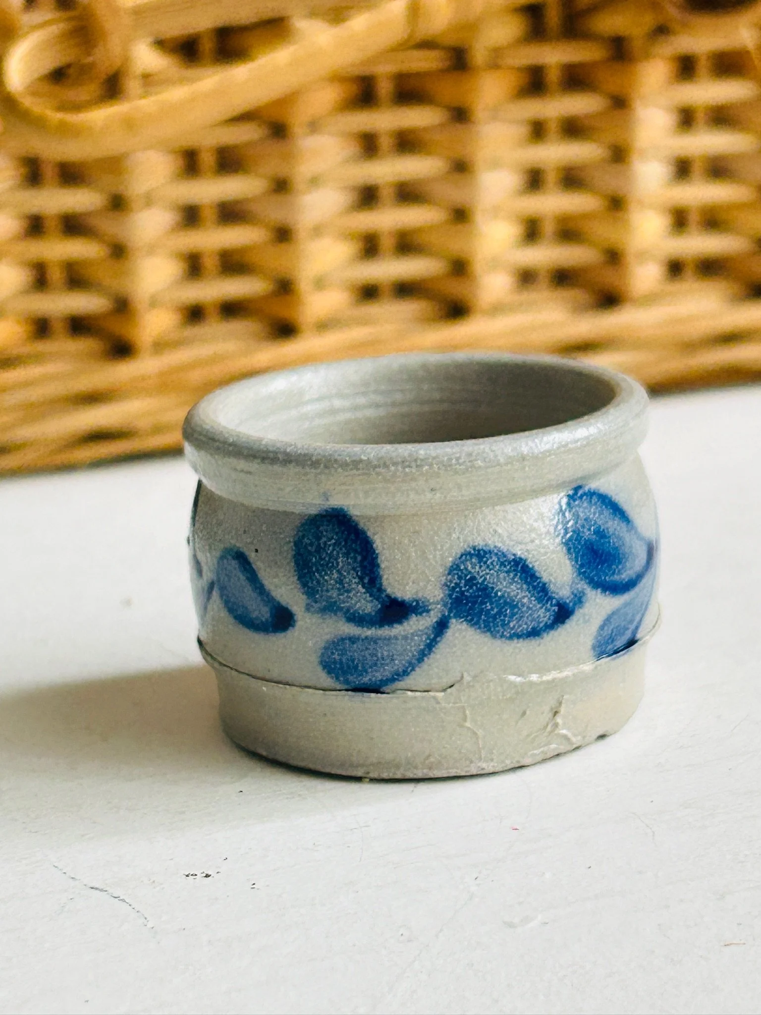 Front view of the handmade stoneware salt cellar with cobalt blue leaf motif on a taupe-grey body, shown against a wicker background