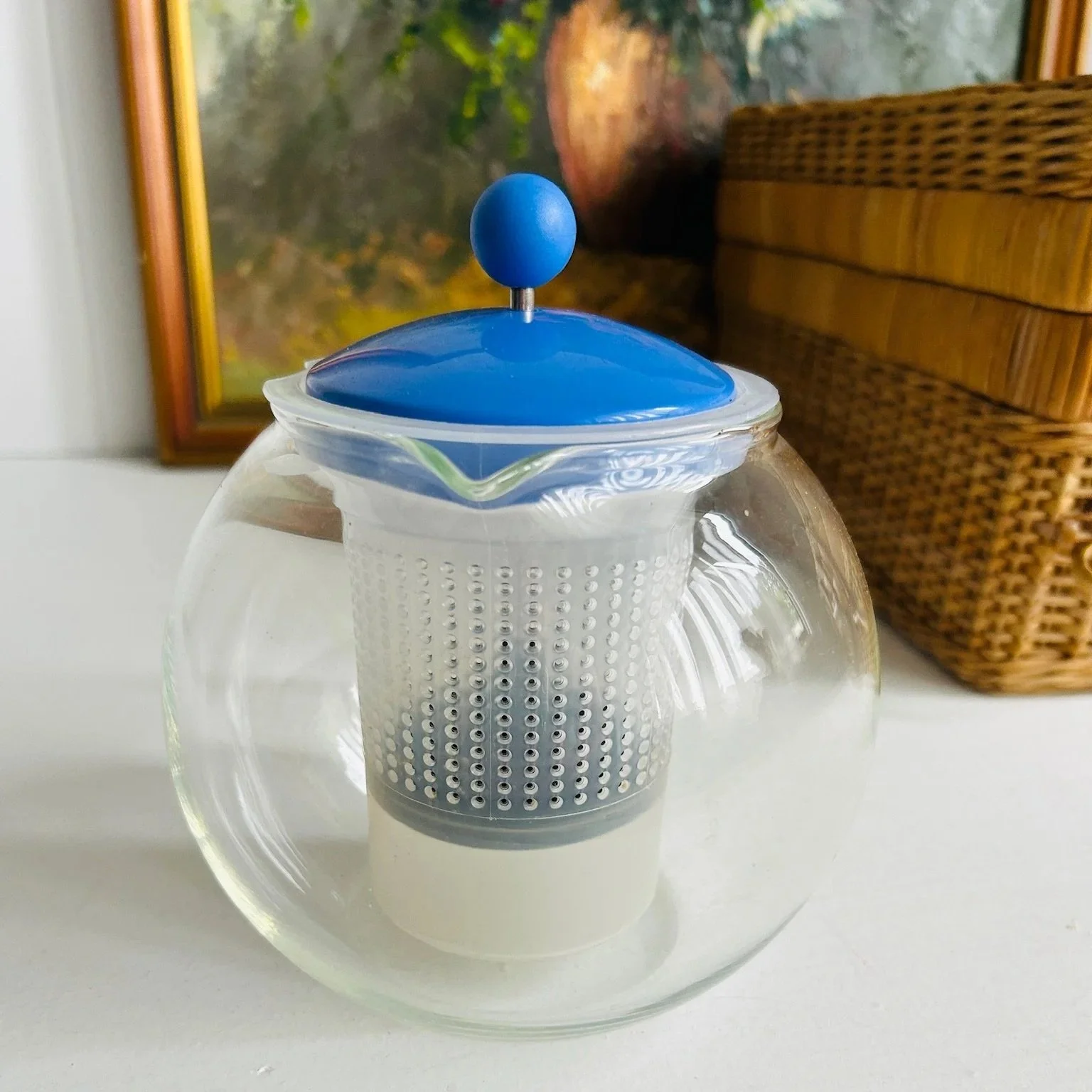 Front view of the teapot highlighting the pouring spout, blue lid, and white mesh infuser inside the glass body.