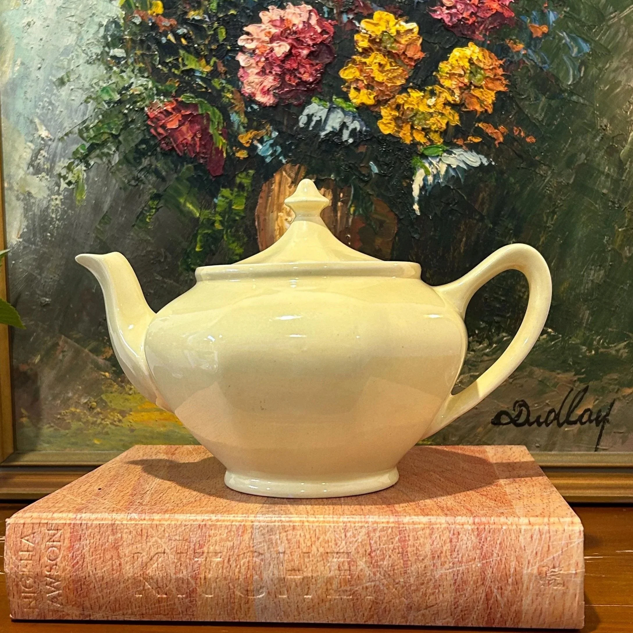 Full view of the Primrosa teapot styled in front of a floral painting on a wooden base