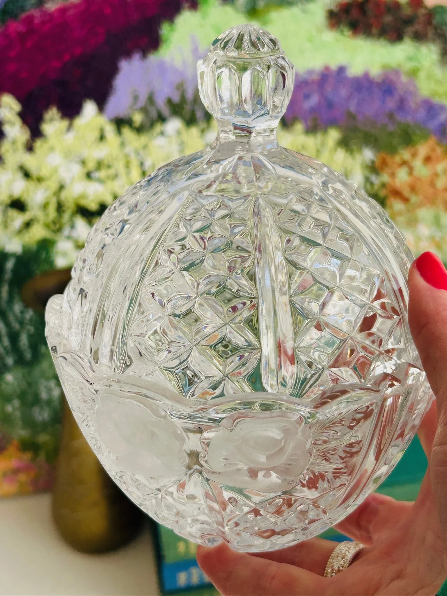 Angled side view of the lidded crystal dish held in hand, showing the frosted rose band, faceted surface, and brilliant sparkle.