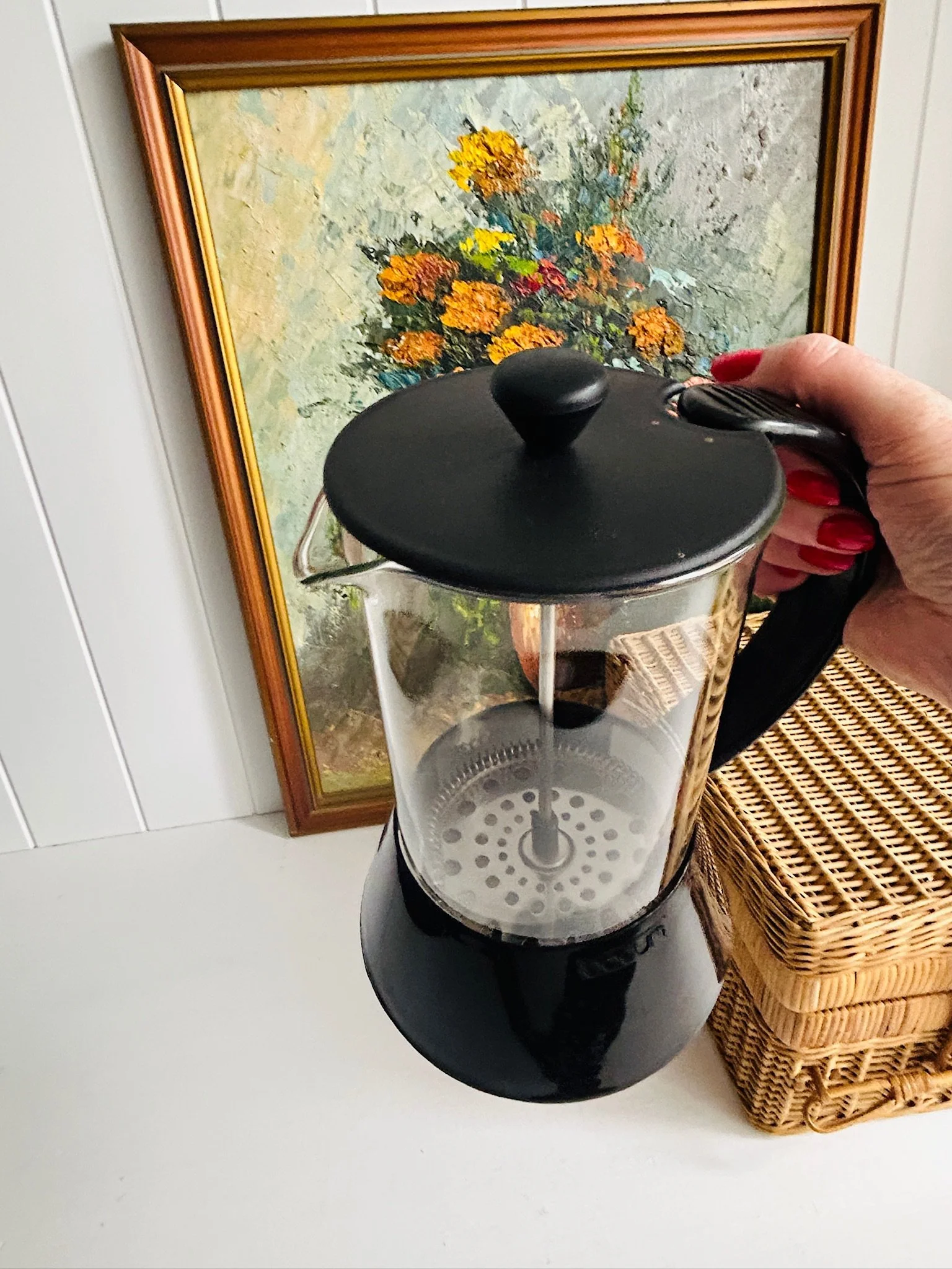 Angled side view of the French press held in hand, highlighting the black lid, curved handle, and glass body.