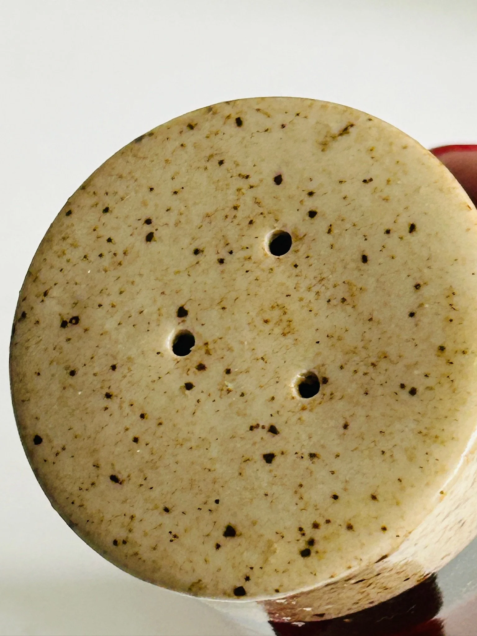 Top view of one shaker showing three dispensing holes in the speckled cream ceramic lid.
