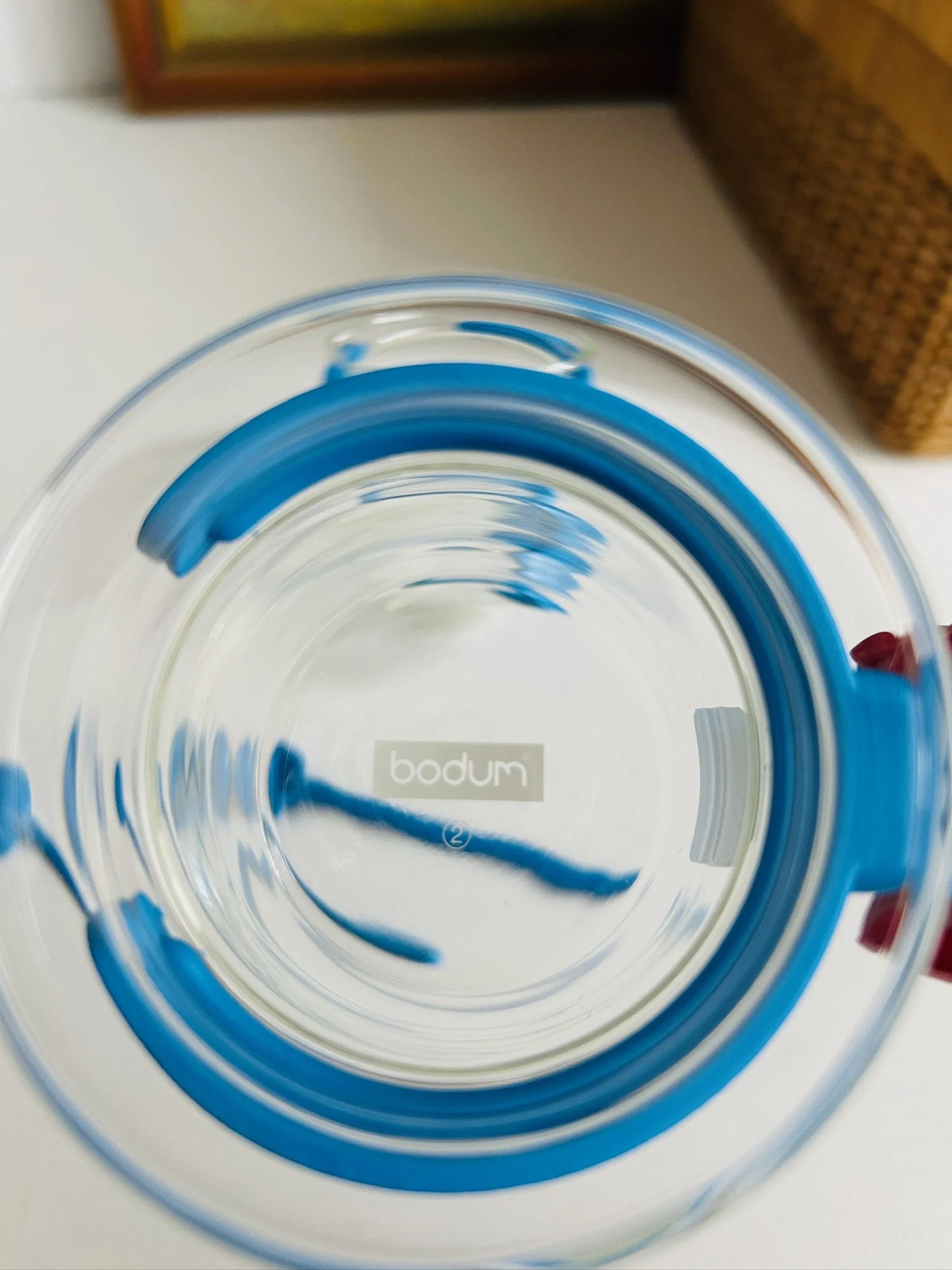 Top-down view into a Bodum Picard cup with blue holder, showing the Bodum logo stamped on the base through the clear glass.