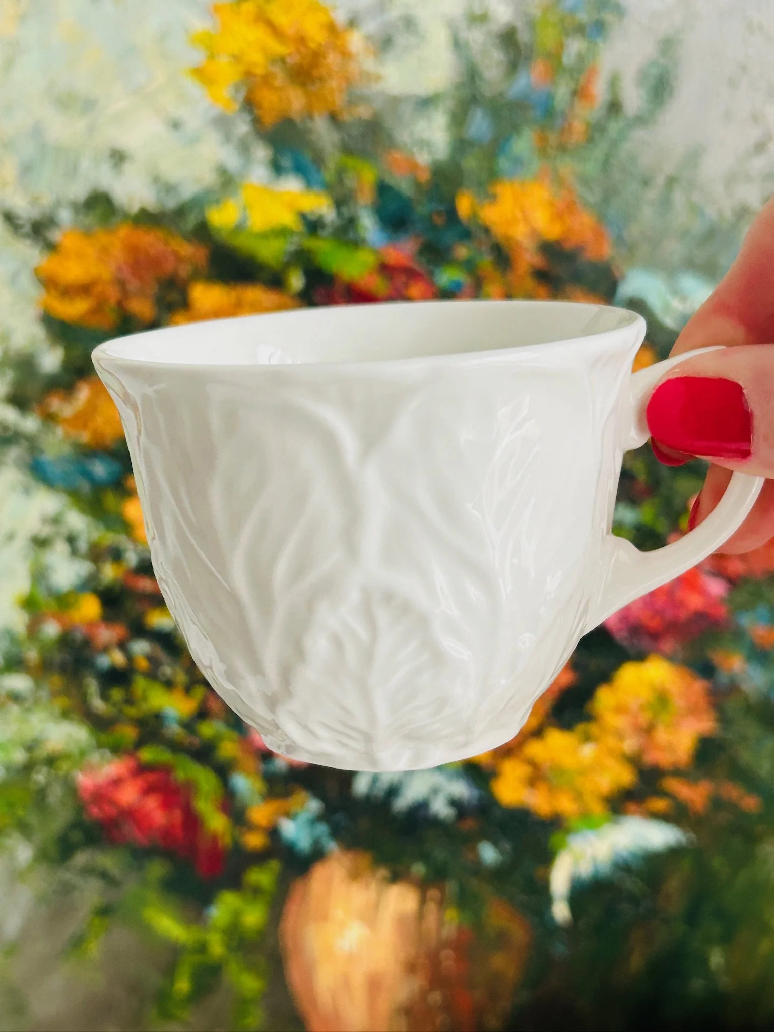 Close-up of the Wedgwood cup held in hand, showing the sculpted leaf pattern and delicate curved handle.