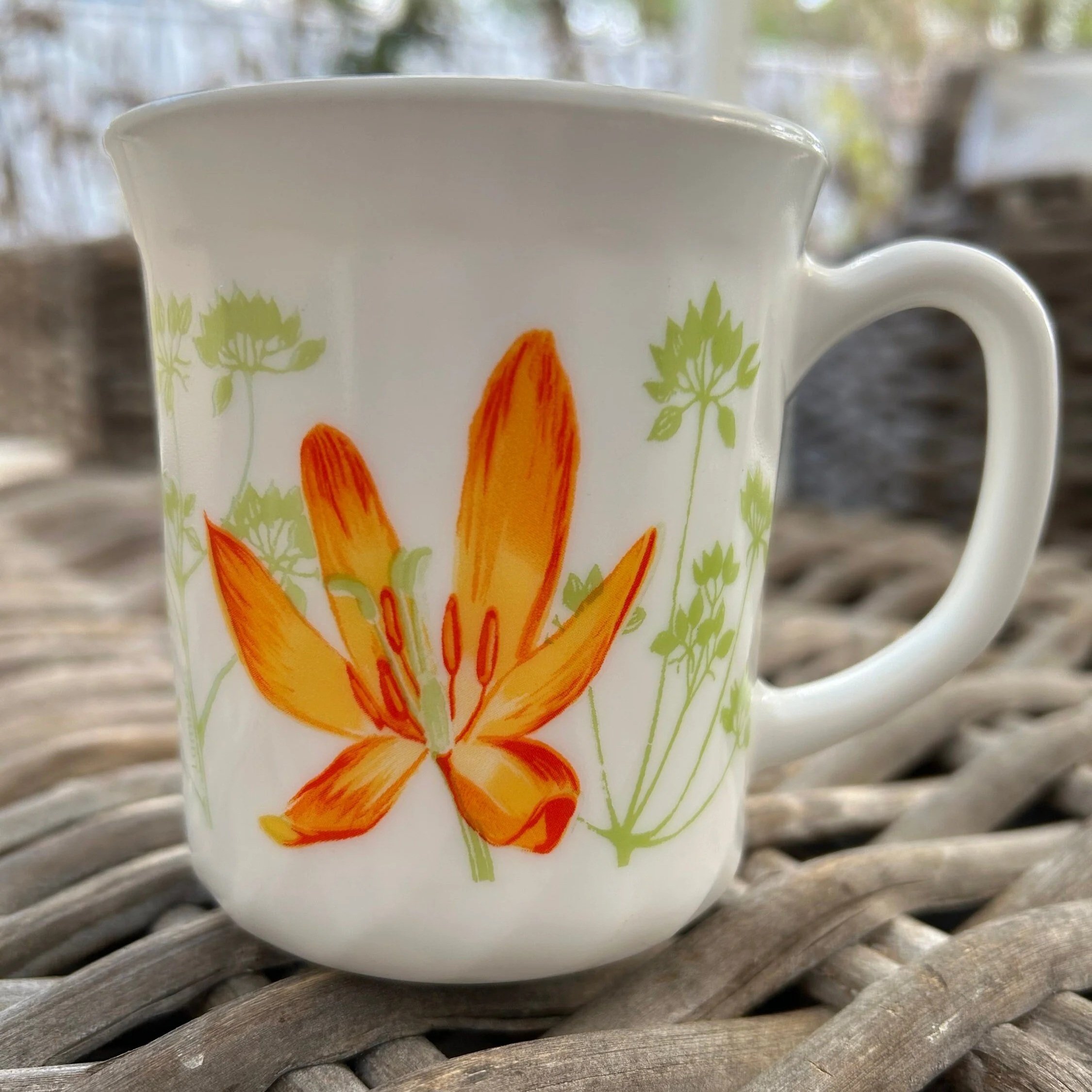 Luminarc milk glass mug with orange floral design on rattan table