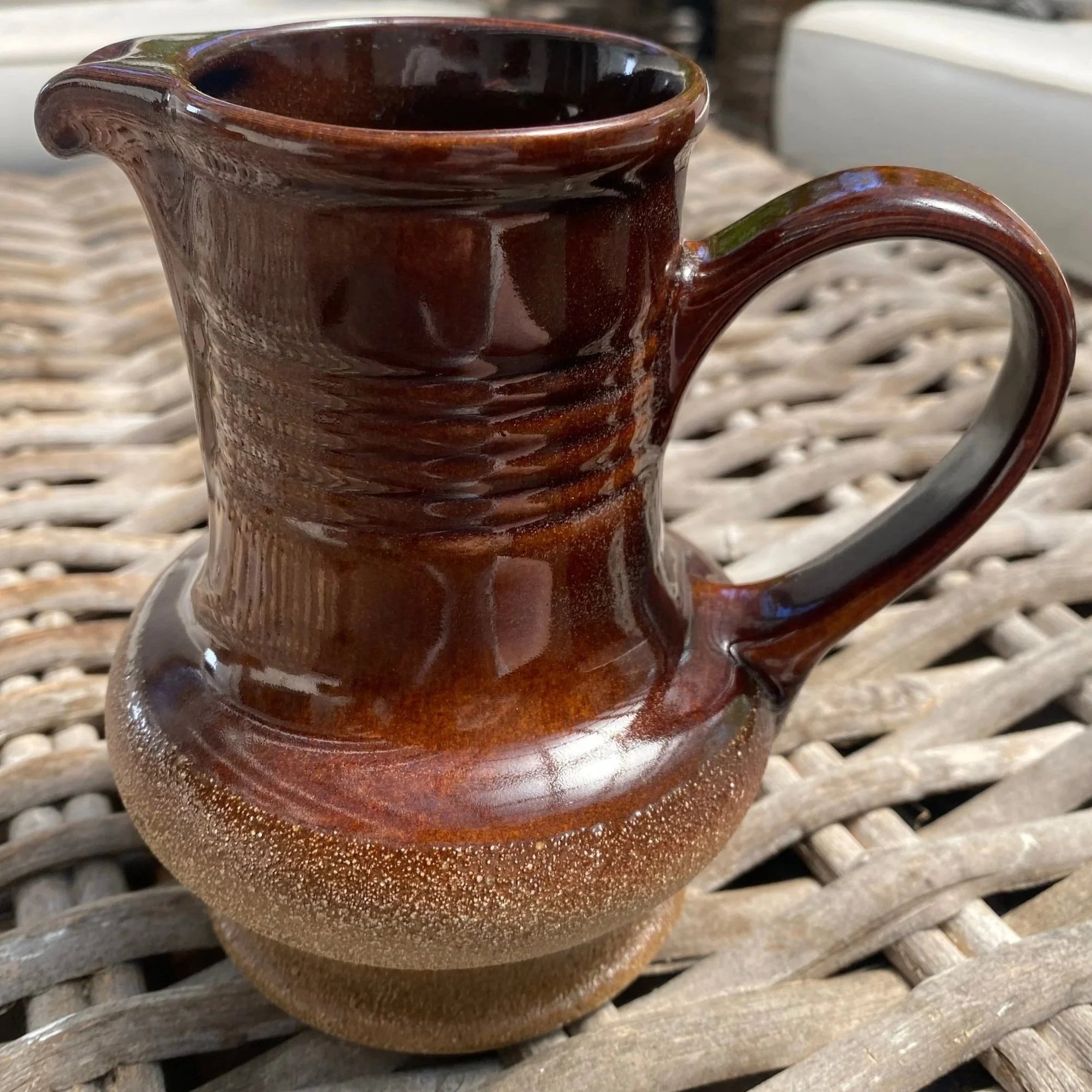 Full front view of vintage brown pottery jug with handle, set on wicker surface