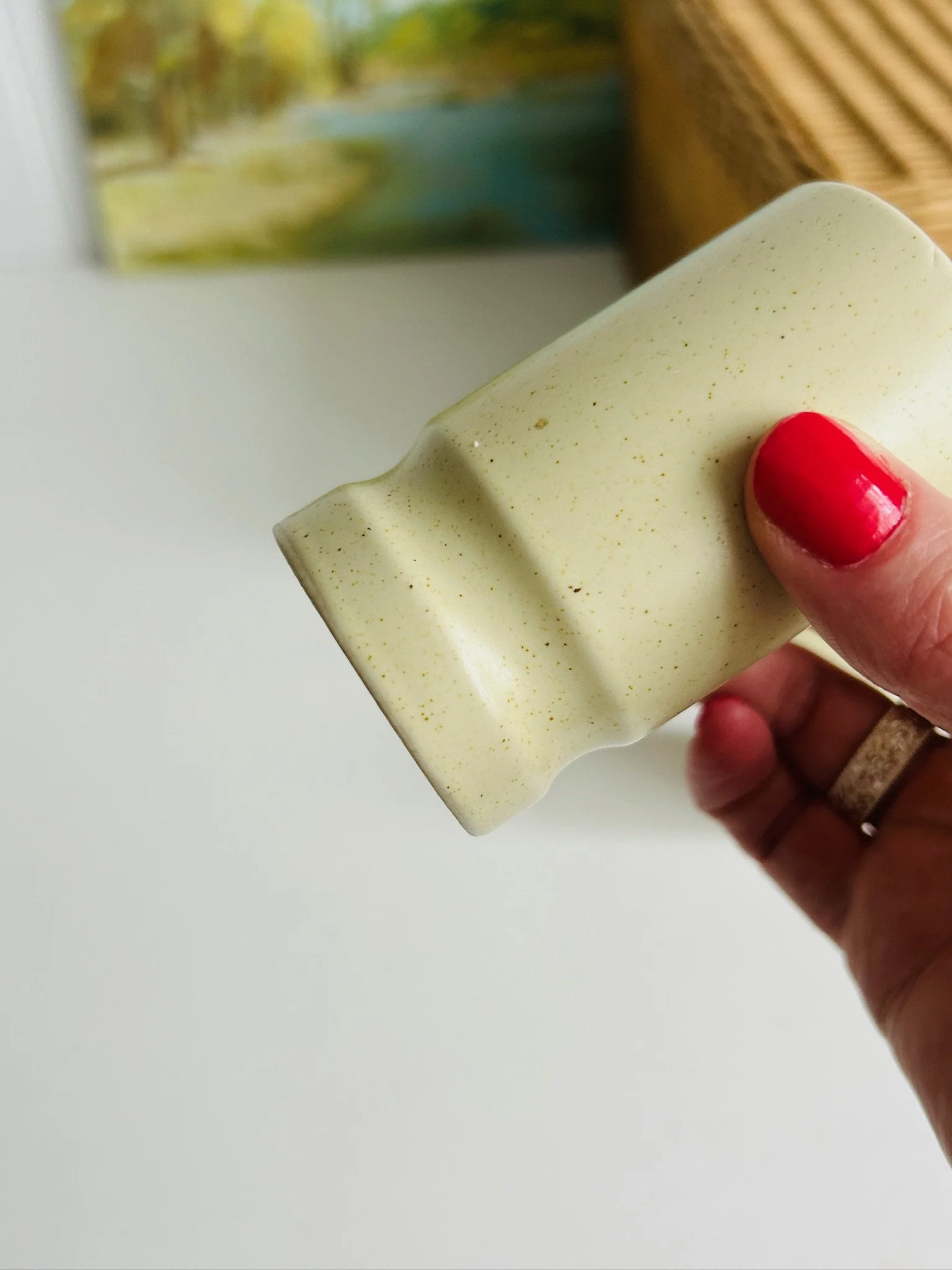 Single shaker held at an angle in hand, showing the lower curve, base ring, and speckled glaze