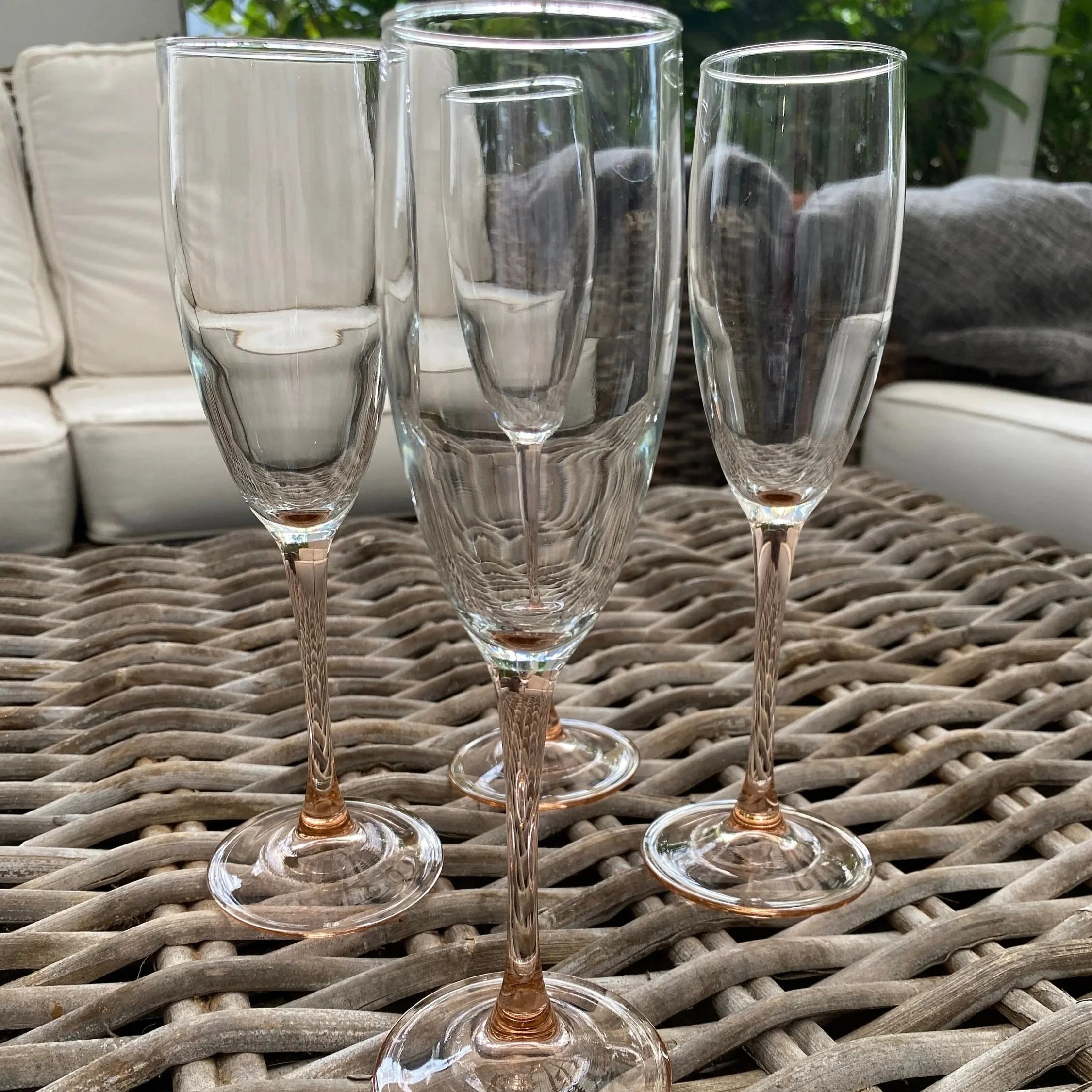 Full set of 4 vintage pink-stemmed champagne flutes on outdoor wicker table