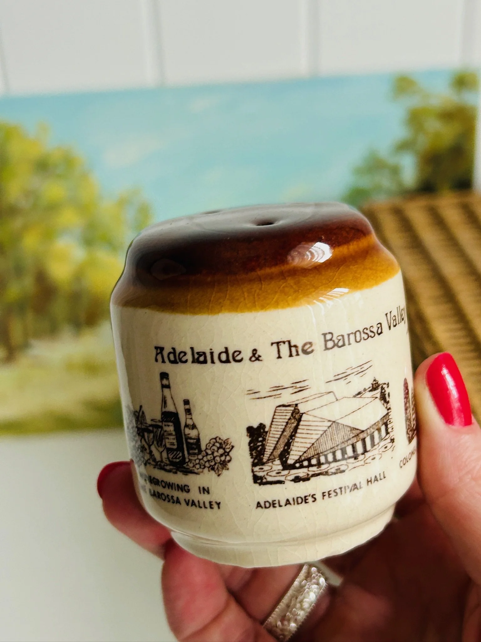Single shaker held in hand, showing the scale, brown drip-glaze top, and Adelaide Festival Hall illustration.