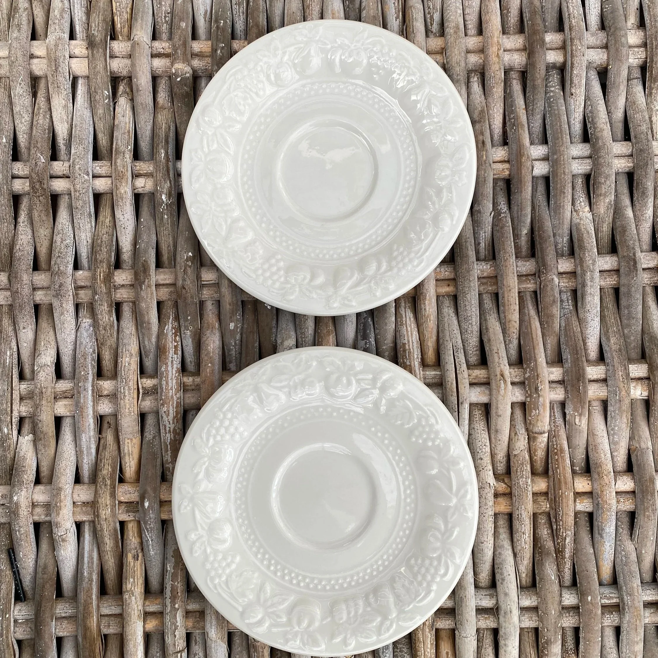 Overhead view of two white Stoneage saucers with raised fruit pattern