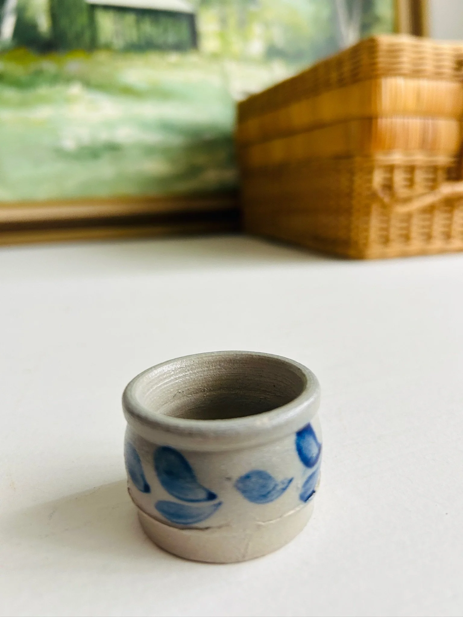 Distant front view of the tiny handmade salt cellar on a white surface beside a wicker basket